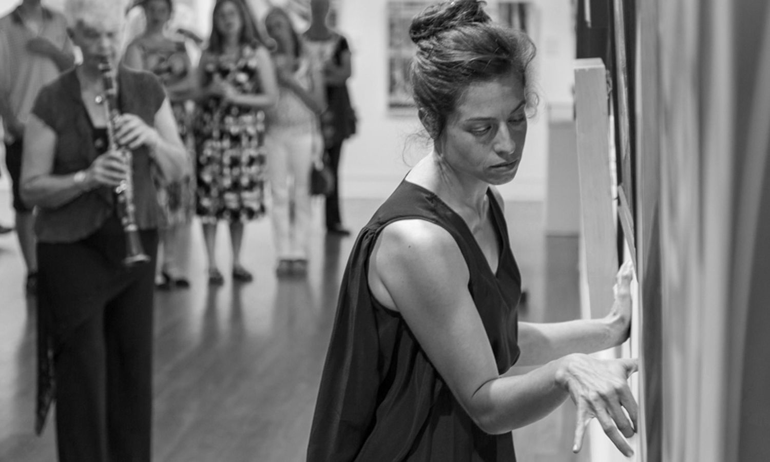 Black and white candid photo of performance artists at a gallery event surrounded by onlookers. Photo by Raymond Mather.