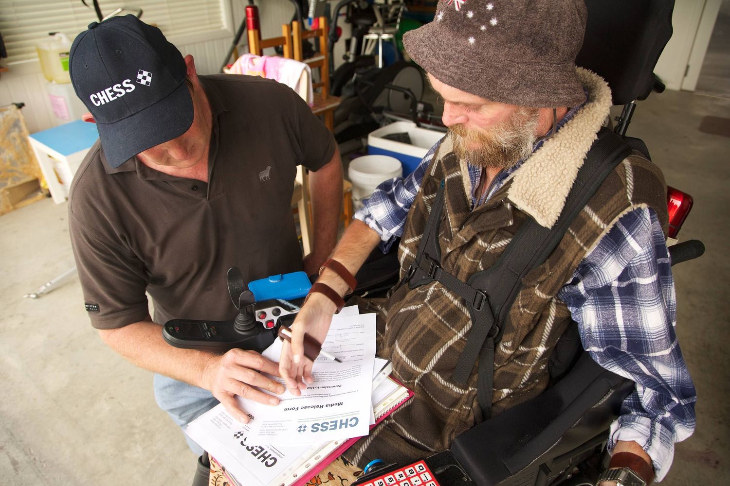 Two men reviewing paperwork, one in mobility chair, representing teamwork, empowerment, CHESS Services. Photo by Raymond Mather.