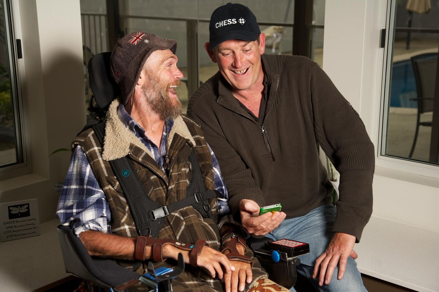 Two men sharing relaxed conversation, laughter, bright interior, companionship, and understanding. CHESS Services. Photo by Raymond Mather.