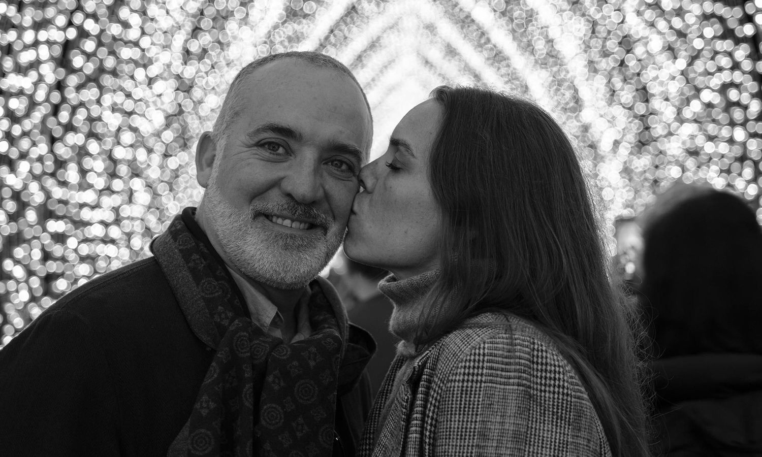 Black and white evening portrait of couple sharing a kiss beneath sparkling tunnel lights of Vivid. Photo by Raymond Mather.