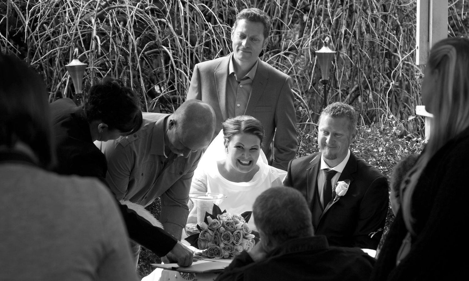 Monochrome image of outdoor ceremony with guests gathered close in intimate celebration. Photo by Raymond Mather.