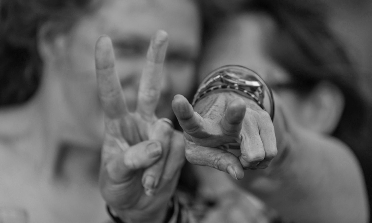 Monochrome artistic photo of two cheeky friends smiling and making a peace sign gesture. Photo by Raymond Mather.