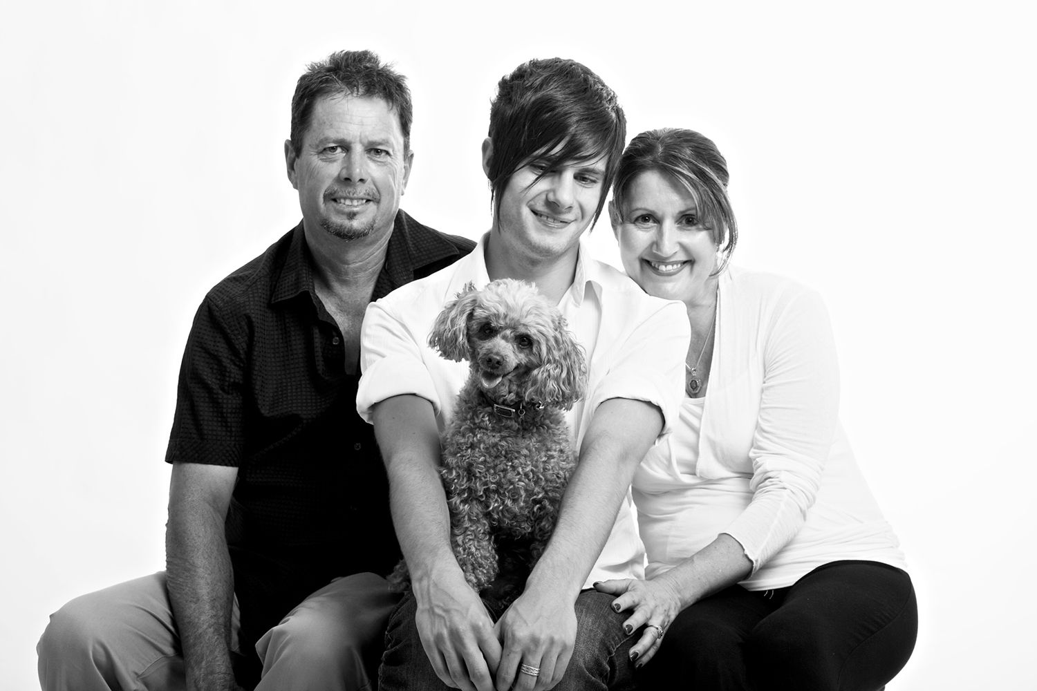 Monochrome studio portrait of family with pet dog, smiling together in relaxed harmony. Photo by Raymond Mather.