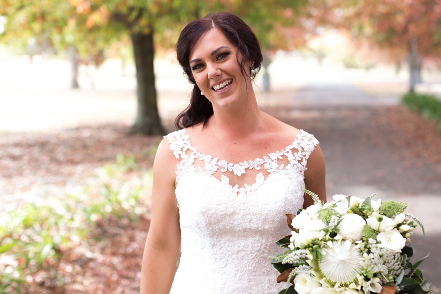 Colour bridal portrait featuring the bride smiling in natural afternoon light with autumn tones in the background. Photo by Raymond Mather.