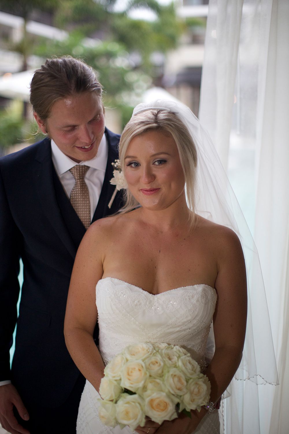 Colour intimate wedding portrait of bride and groom standing together by the water. Photo by Raymond Mather.