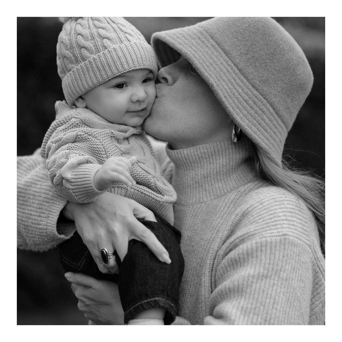 Monochrome close-up of mother holding baby lovingly in cosy winter clothing. Photo by Raymond Mather.