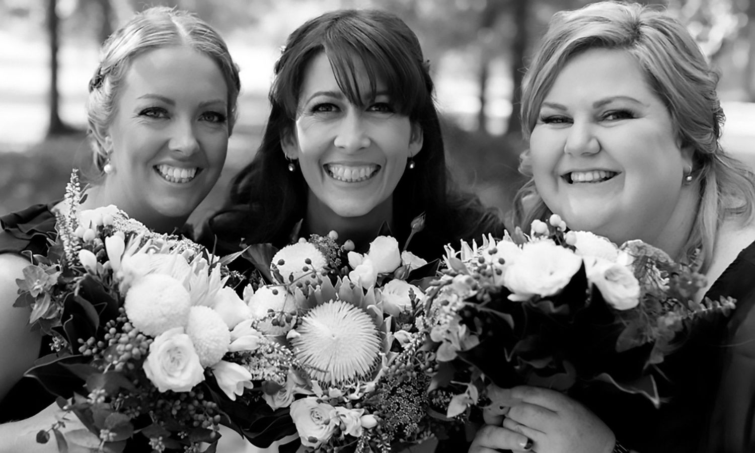 Monochrome close-up of bride and bridesmaids holding bouquets, sharing laughter and connection. Photo by Raymond Mather.