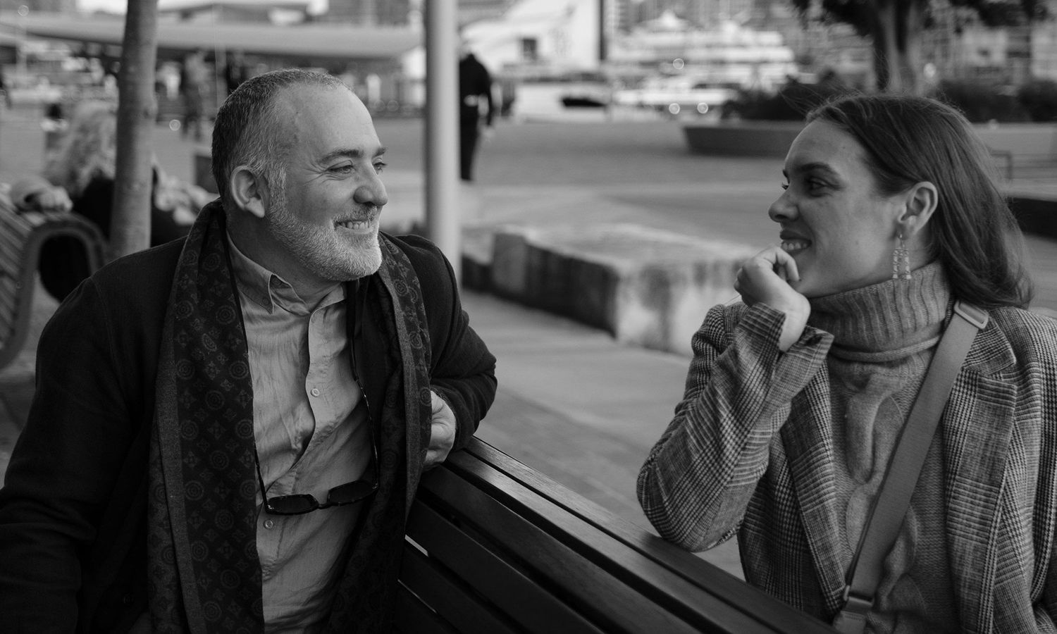 Monochrome candid image of couple laughing together at an outdoor café by the harbour. Photo by Raymond Mather.