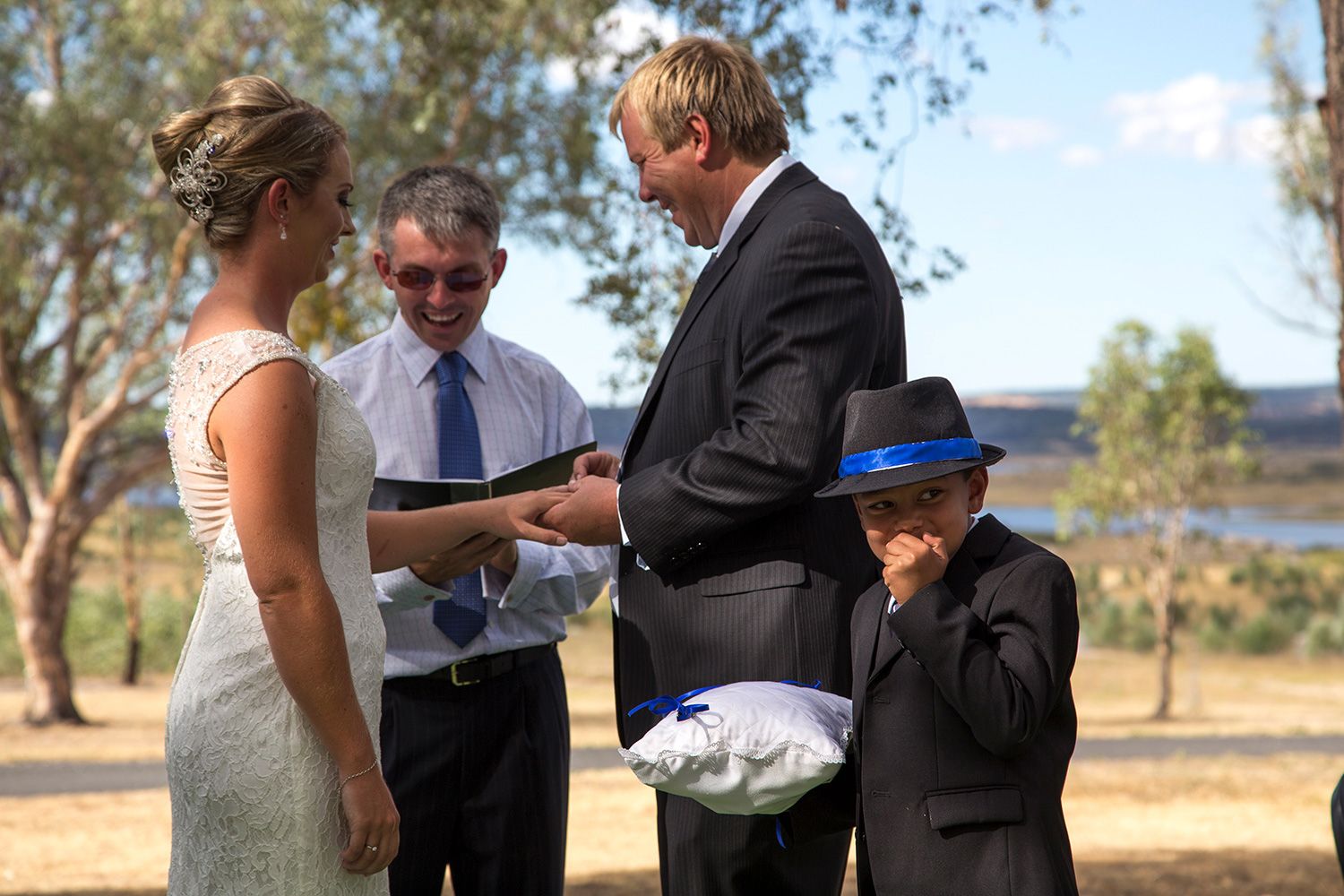 Colour outdoor wedding ceremony photo with couple exchanging vows under warm sunlight. Photo by Raymond Mather.
