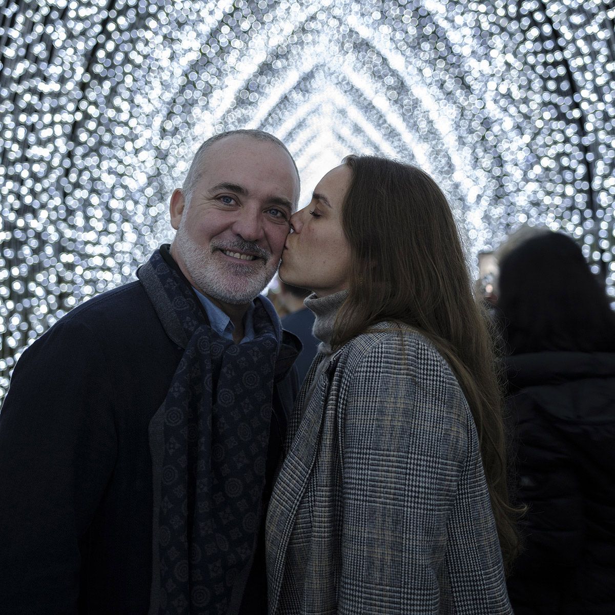 Colour evening portrait of couple sharing a kiss beneath Vivid sparkling light tunnel in Sydney. Photo by Raymond Mather.