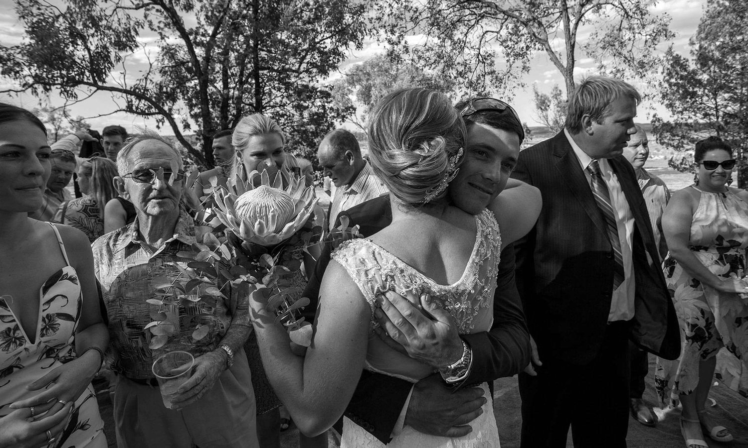 Black and white candid image of newlyweds surrounded by family and friends after the ceremony. Photo by Raymond Mather.