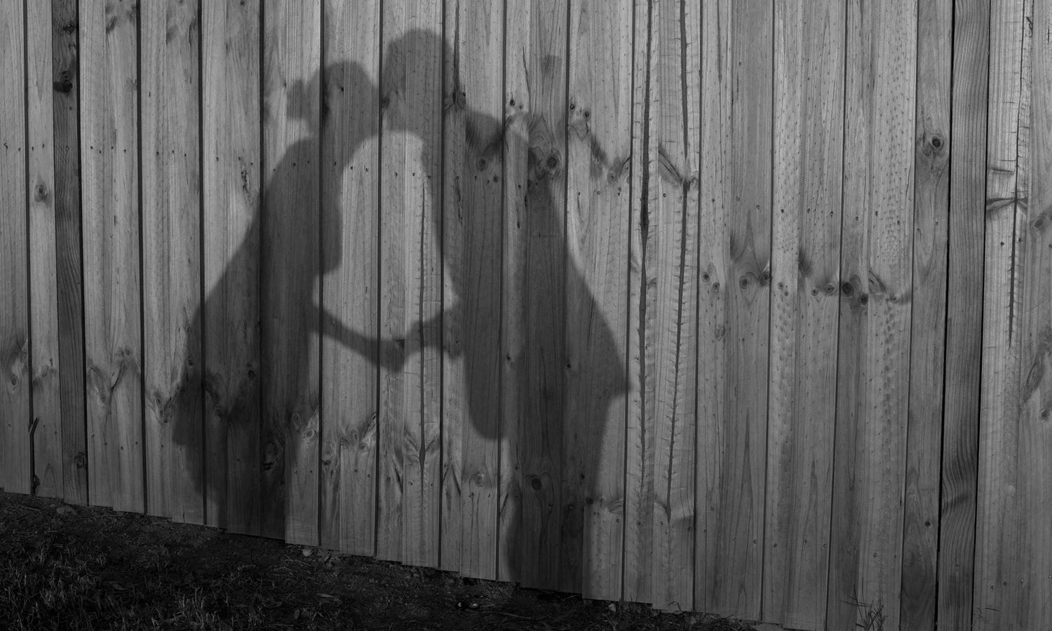 Silhouettes of people posing playfully against a wooden fence at dusk. Photography by Raymond Mather.