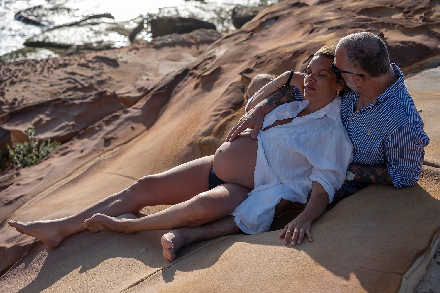 Expectant couple resting on sandstone, tenderness wrapped in golden calm. Photo by Raymond Mather.