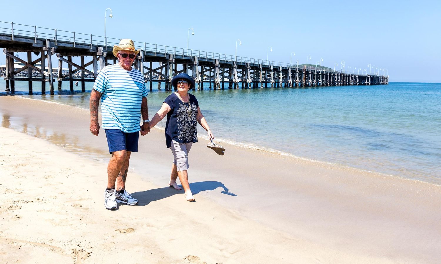 A mature couple walking barefoot along the beach, celebrating family connection and active living. Photo by Raymond Mather.