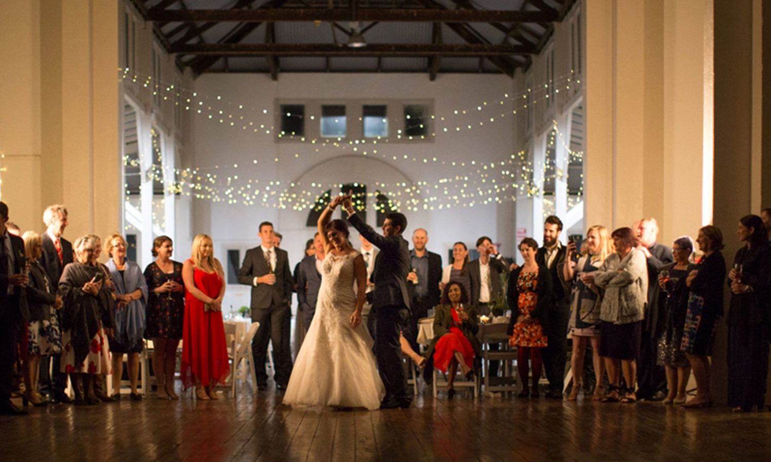 Wedding reception, twinkling lights elegant venue. Newlyweds’ first dance, light, laughter, and shared celebration. Photo by Raymond Mather.