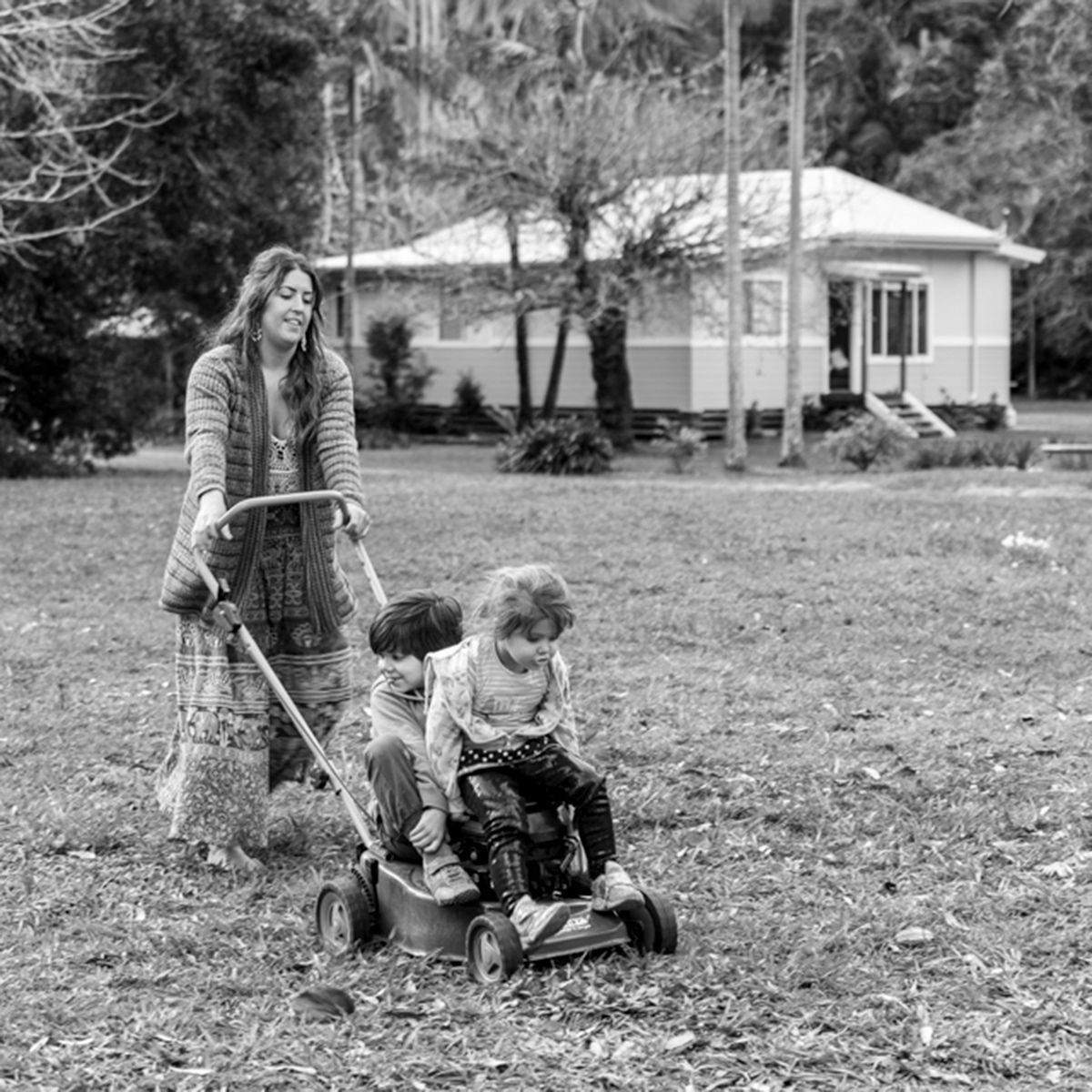 Monochrome candid photo of a family playing on the grass near a country house. Photo by Raymond Mather.