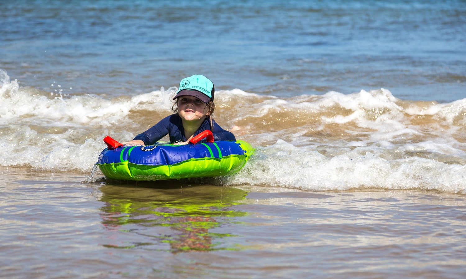 Colour image of a young child riding the waves on a boogie board, symbolising early confidence and play in nature. Photo by Raymond Mather.