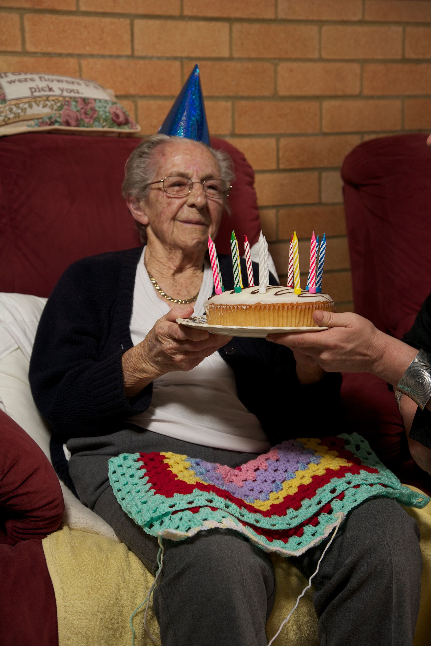 Colour portrait capturing a joyful birthday moment as an elderly woman receives a cake surrounded by love. Photo by Raymond Mather.