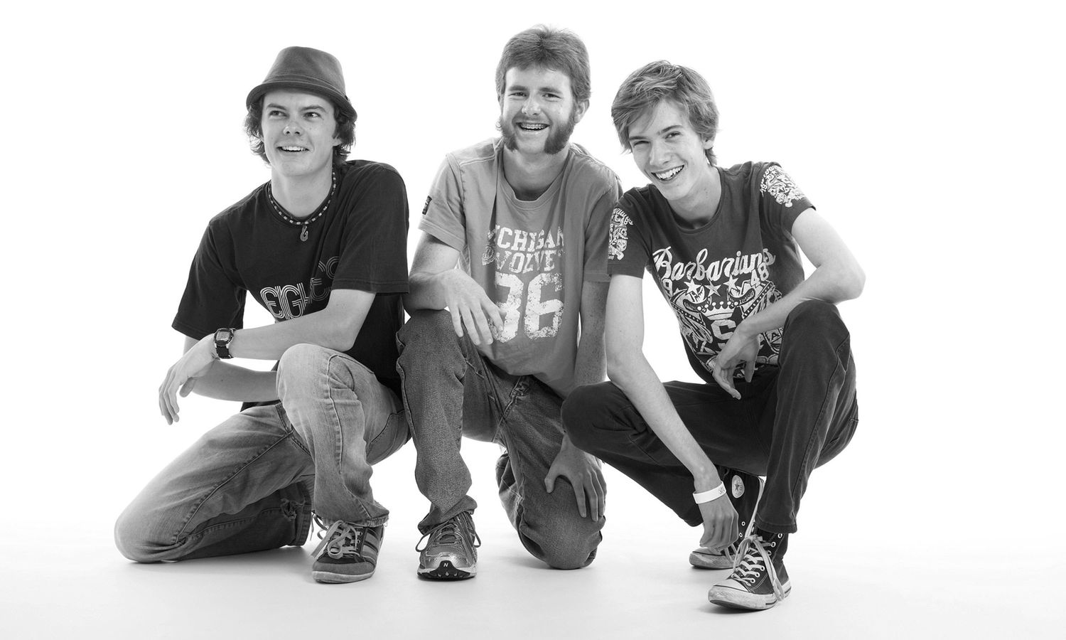 Black and white studio portrait of three young men smiling with relaxed, friendly energy. Photo by Raymond Mather.