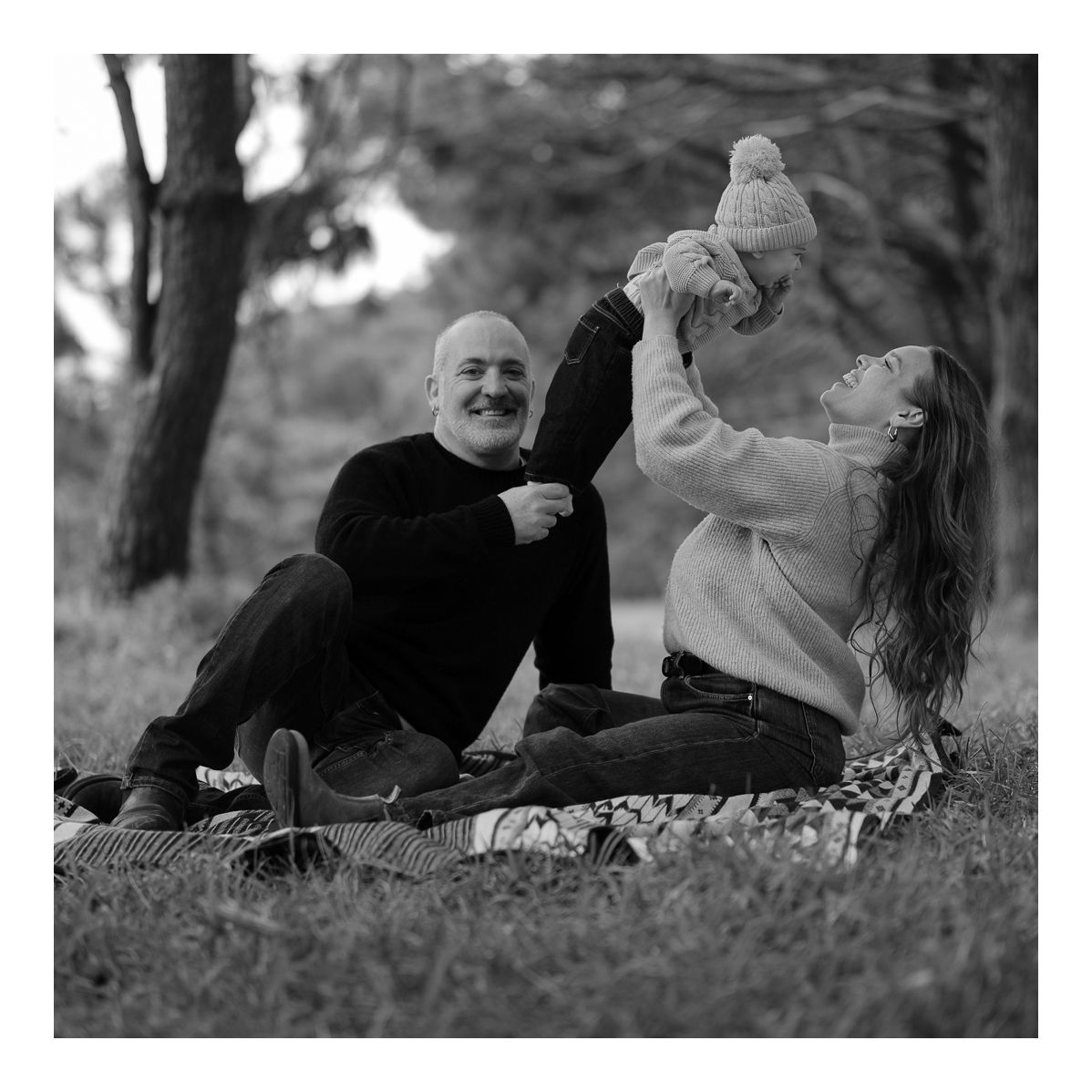 Black and white candid outdoor photo of family laughing together on a picnic rug. Photo by Raymond Mather.