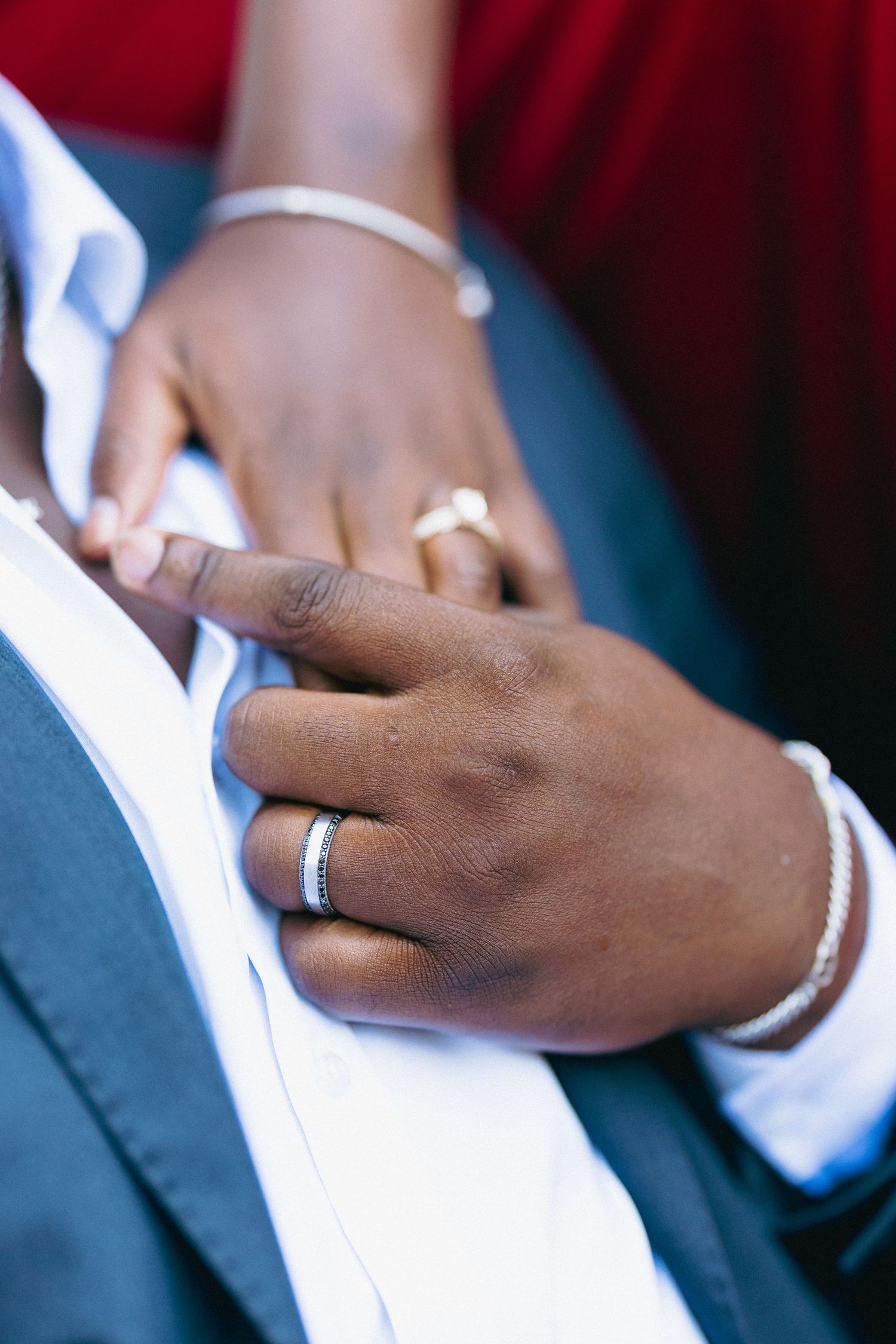 Close-up of two hands with wedding rings touching a groom's white shirt, symbolizing a loving couple's bond.