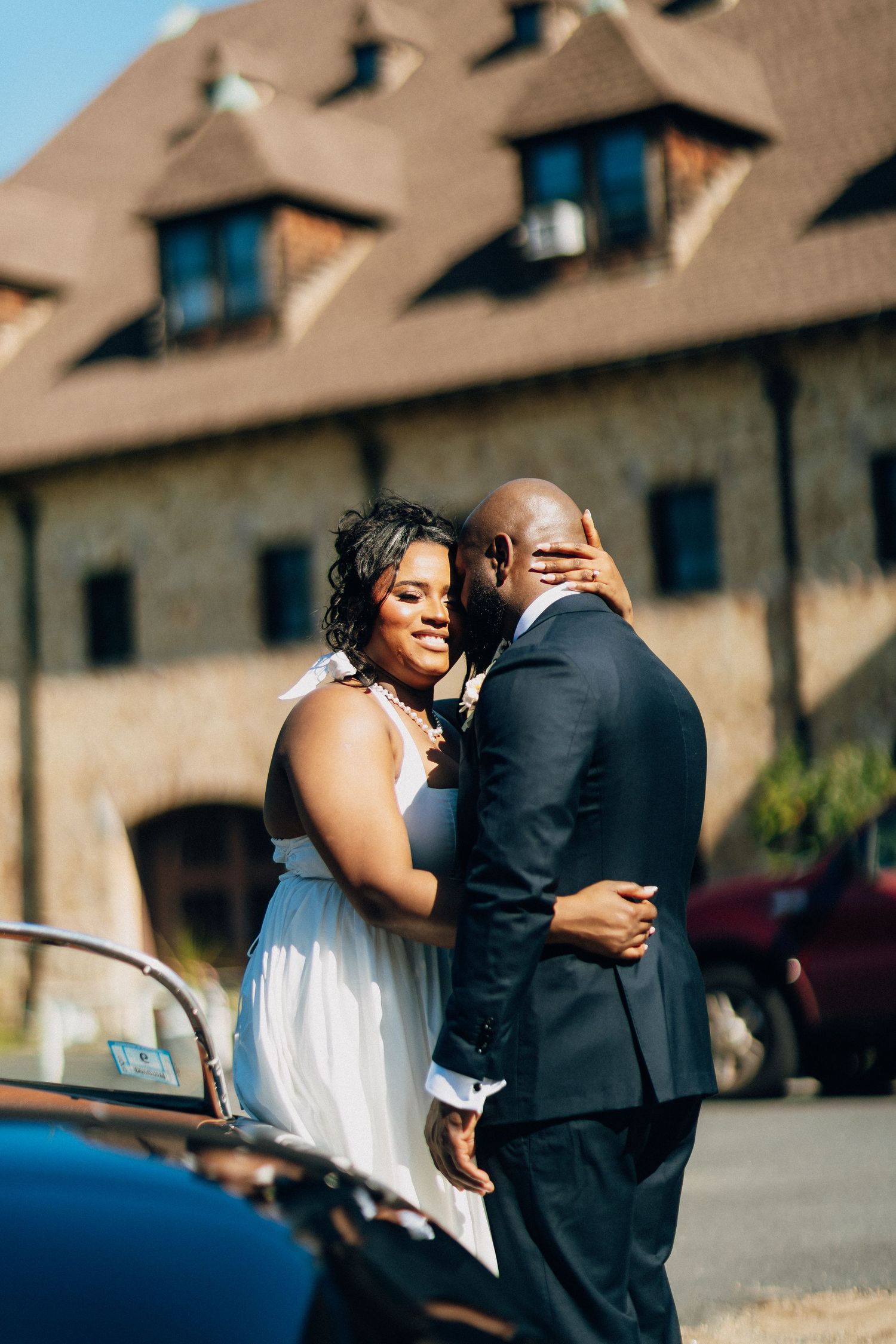 Bride and groom share tender embrace outside rustic stone building on their wedding day.