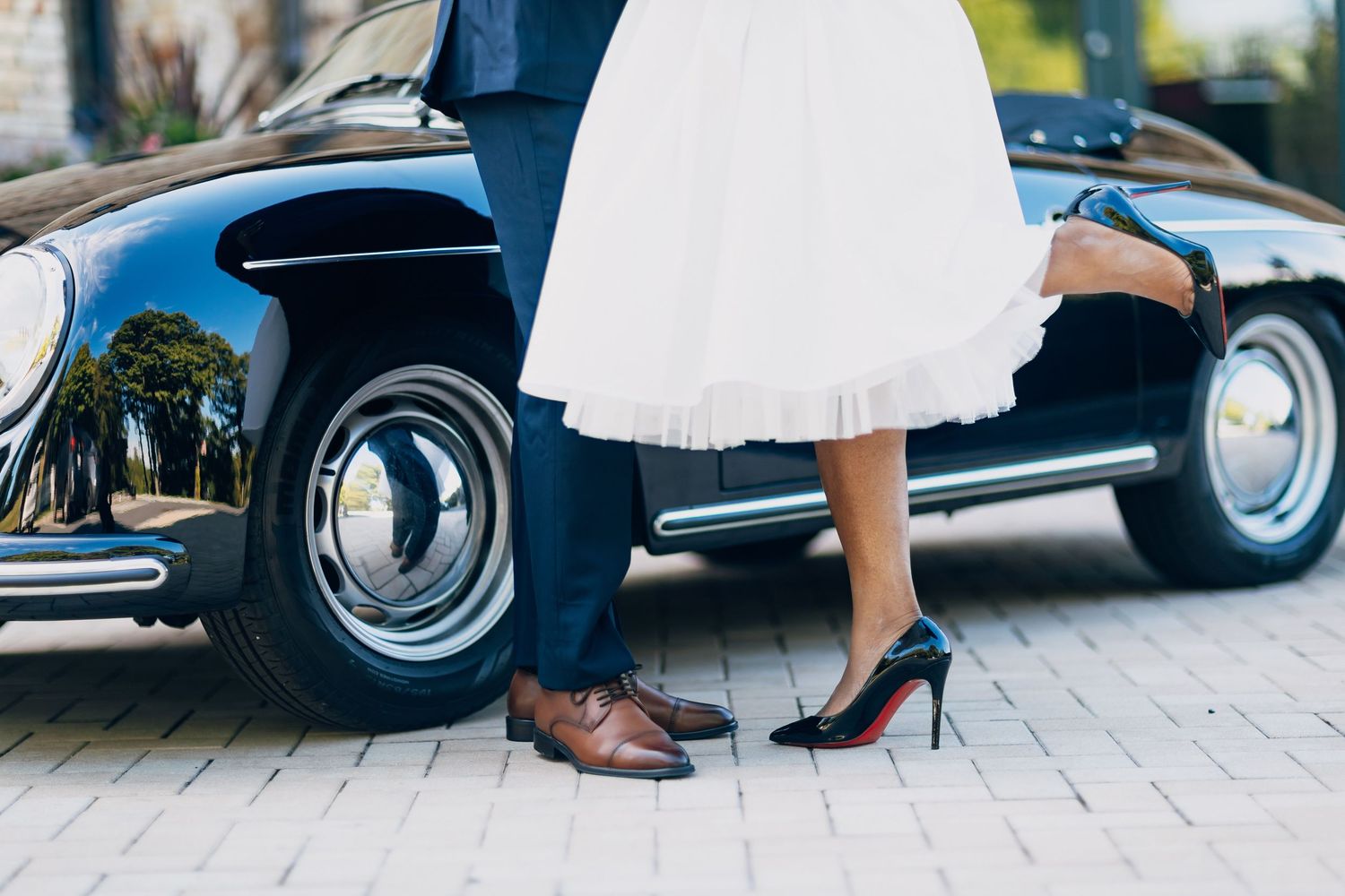 Close-up of bride and groom's feet near a vintage black car, she wearing black heels.