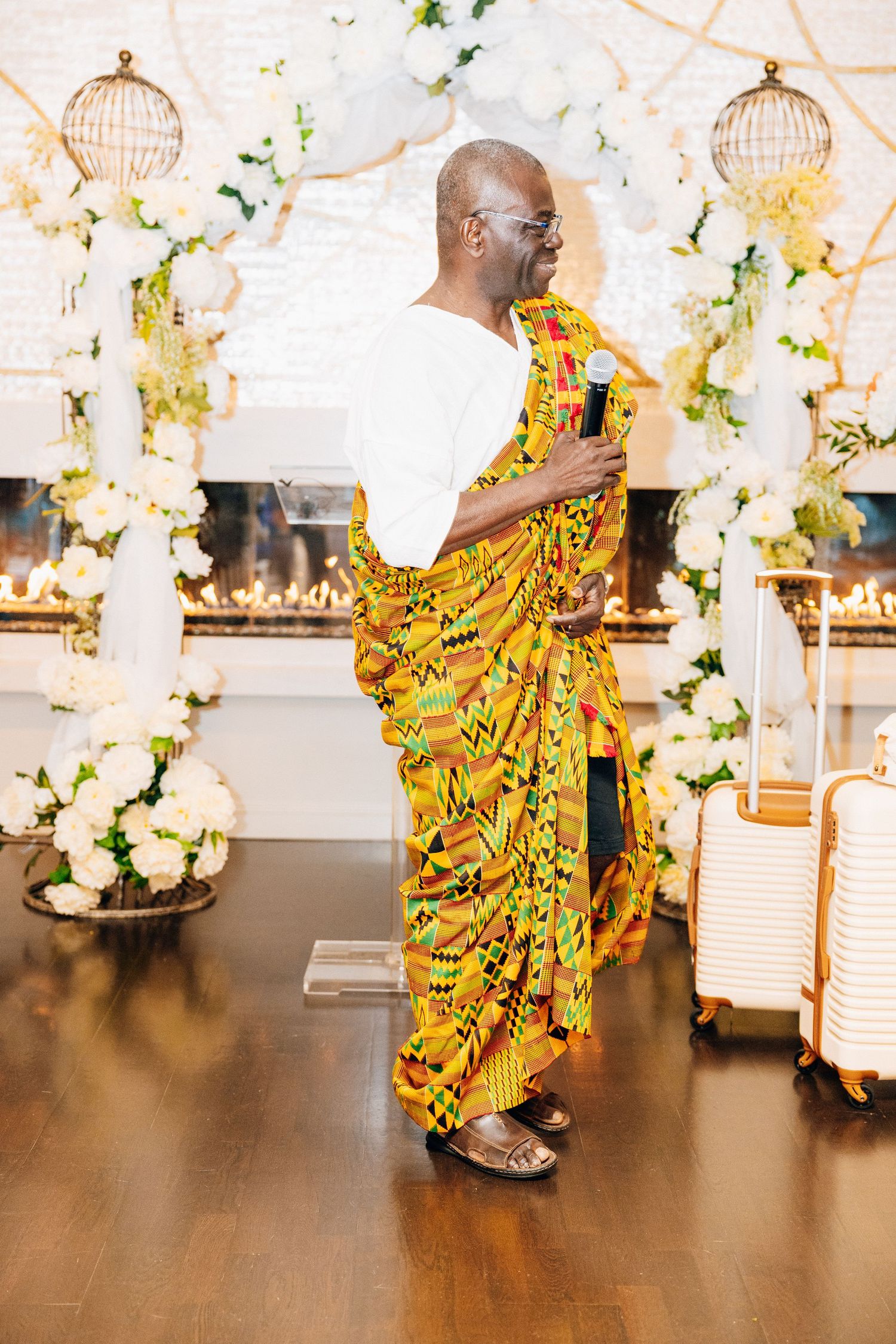 Man in traditional African kente cloth speaking at wedding ceremony with microphone.