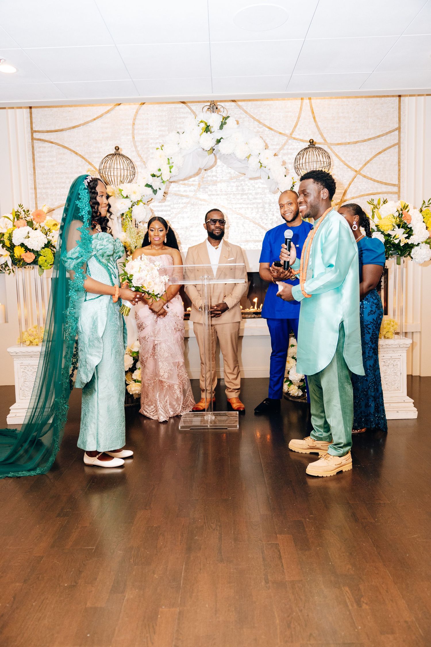 Wedding ceremony with bridal party in teal and mint outfits at decorated altar with floral arch.