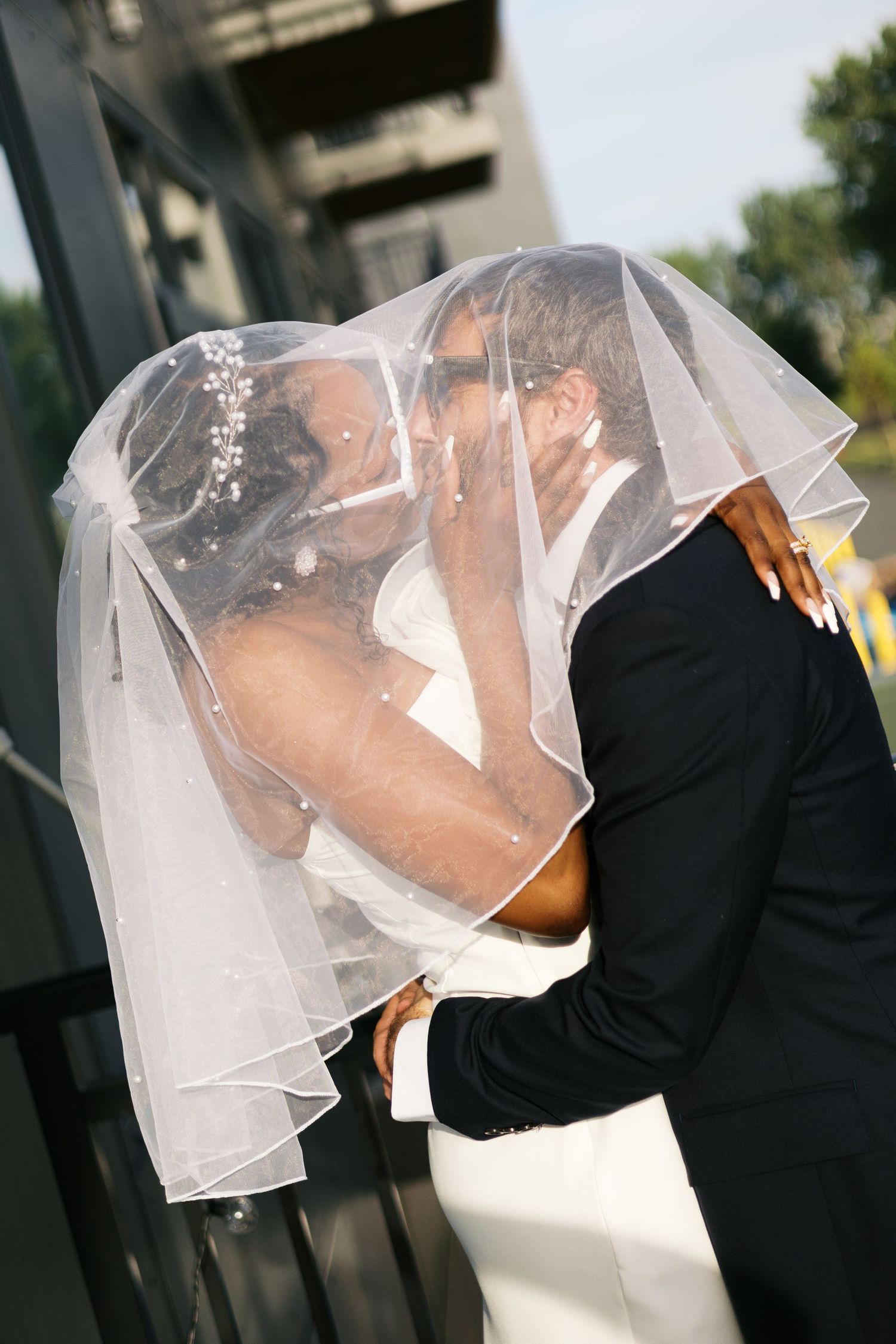 Newlywed couple shares romantic kiss under bride's veil outdoors on their wedding day.