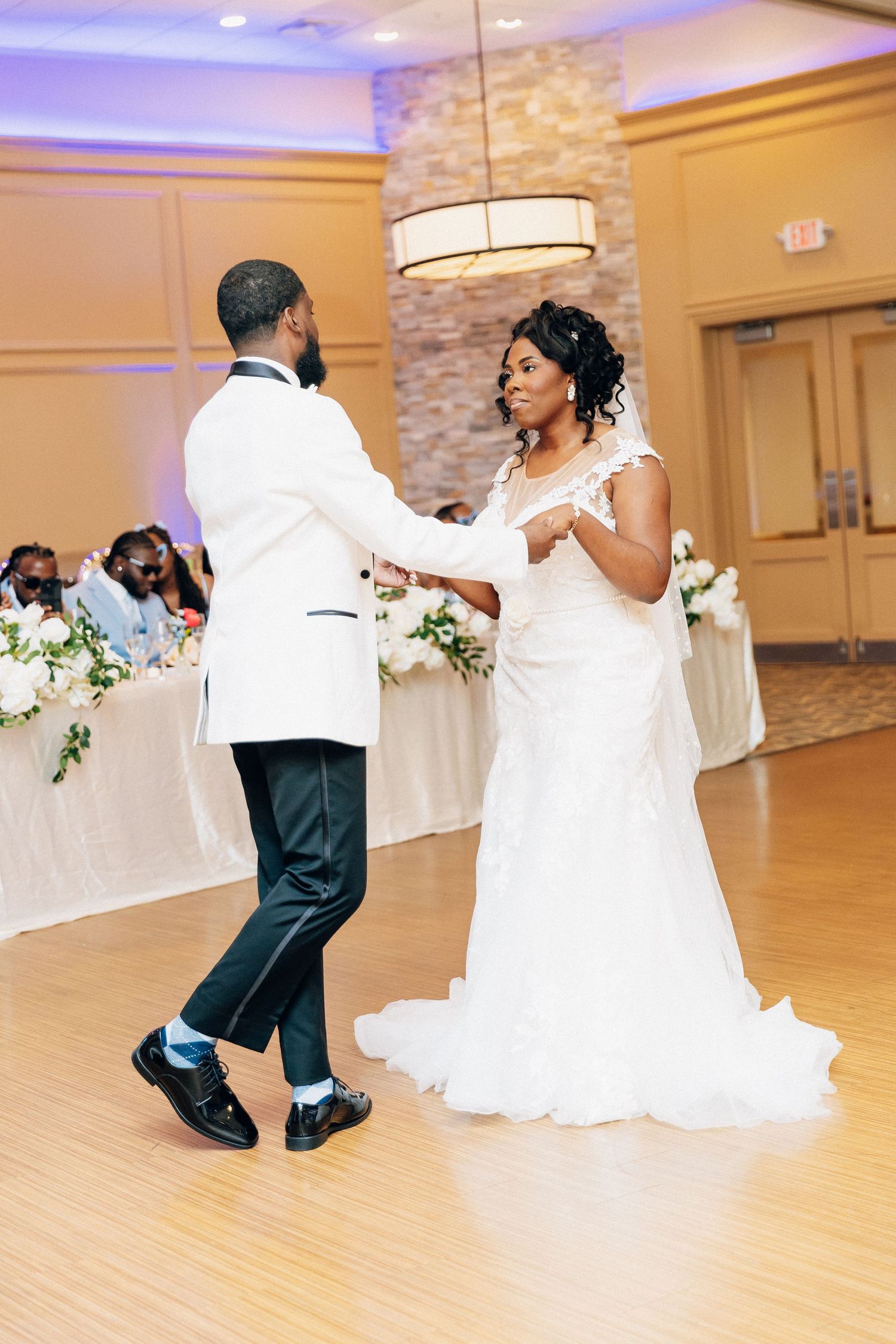 Bride in white lace gown and groom in white tuxedo sharing their first dance at wedding reception.