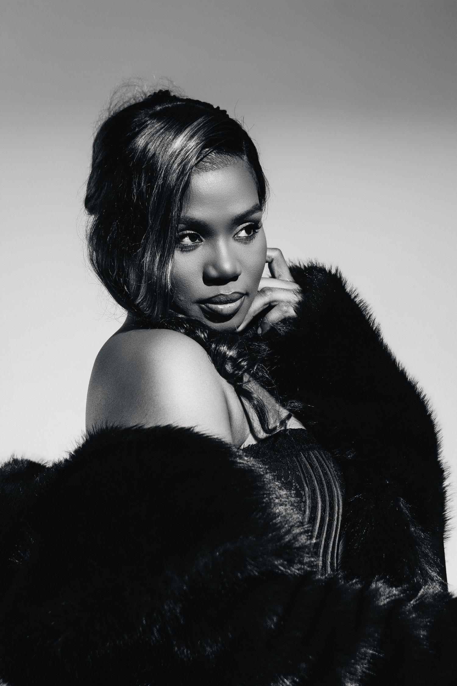 Black and white portrait of a woman in a fur coat posing elegantly with hand near face.