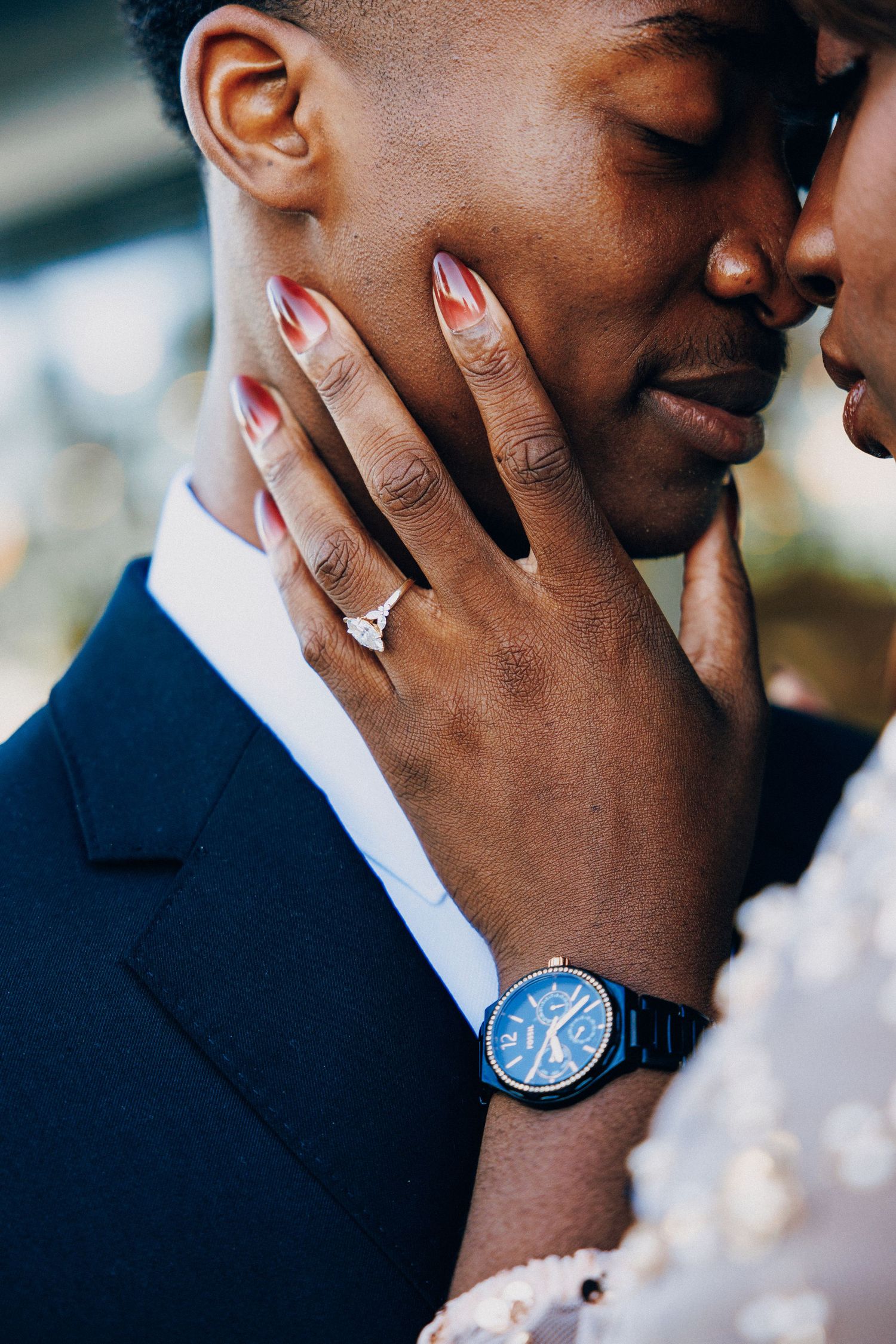 Close-up of bride's hand with diamond ring and blue watch tenderly touching groom's face on wedding day.