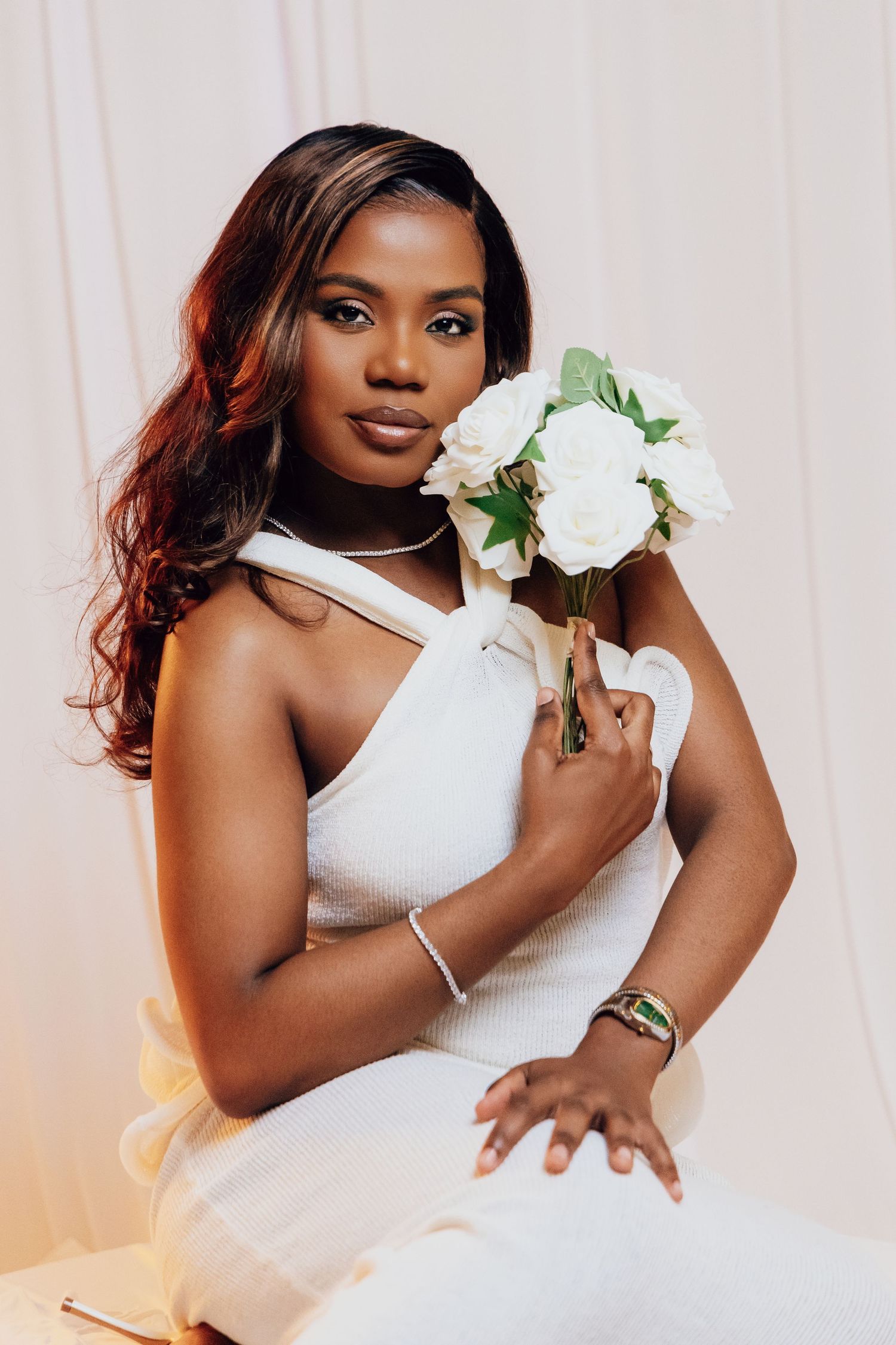 Beautiful Black woman in white halter dress posing with white rose bouquet, wearing silver jewelry.