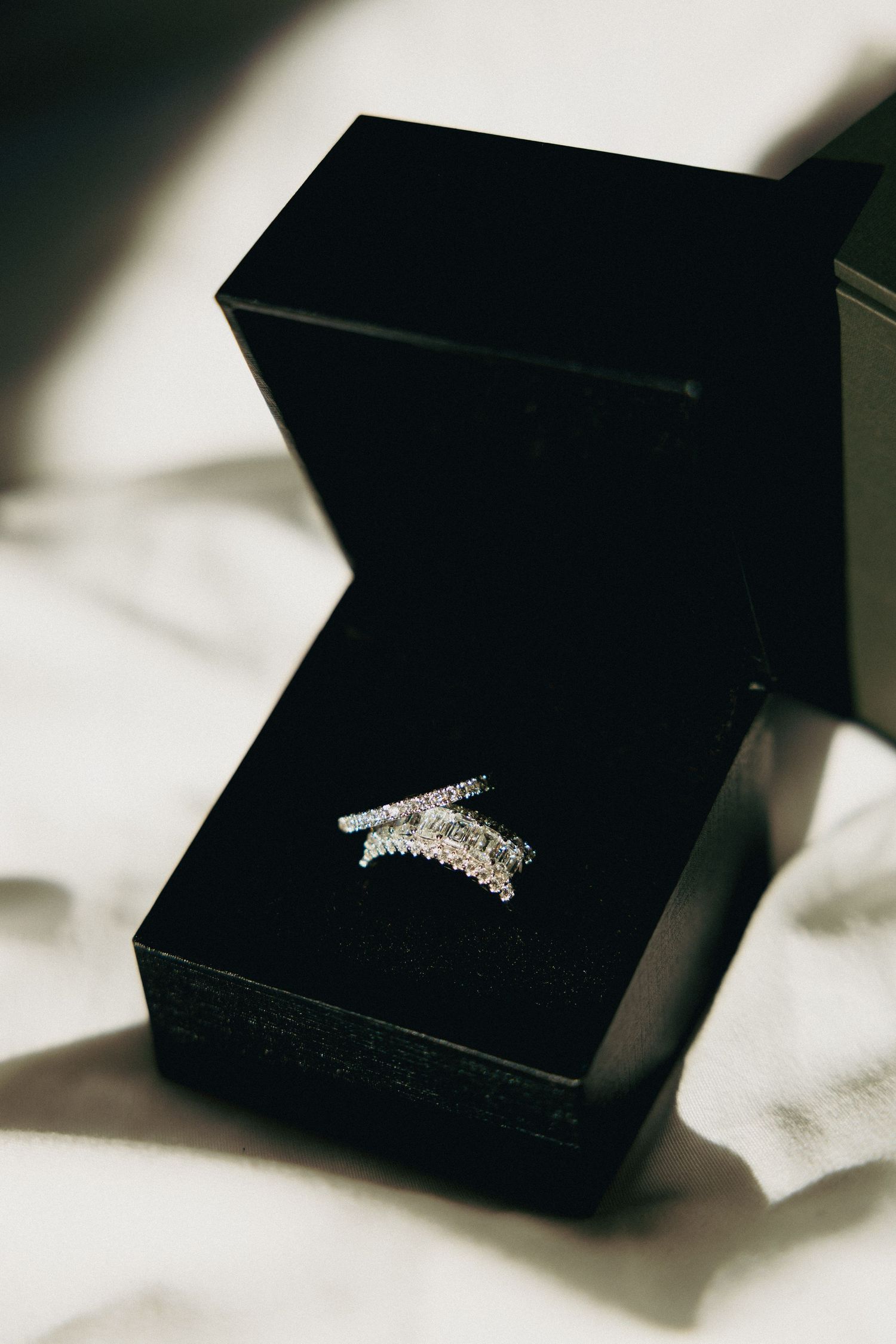 Silver diamond crown ring displayed in a black jewelry box on white fabric.
