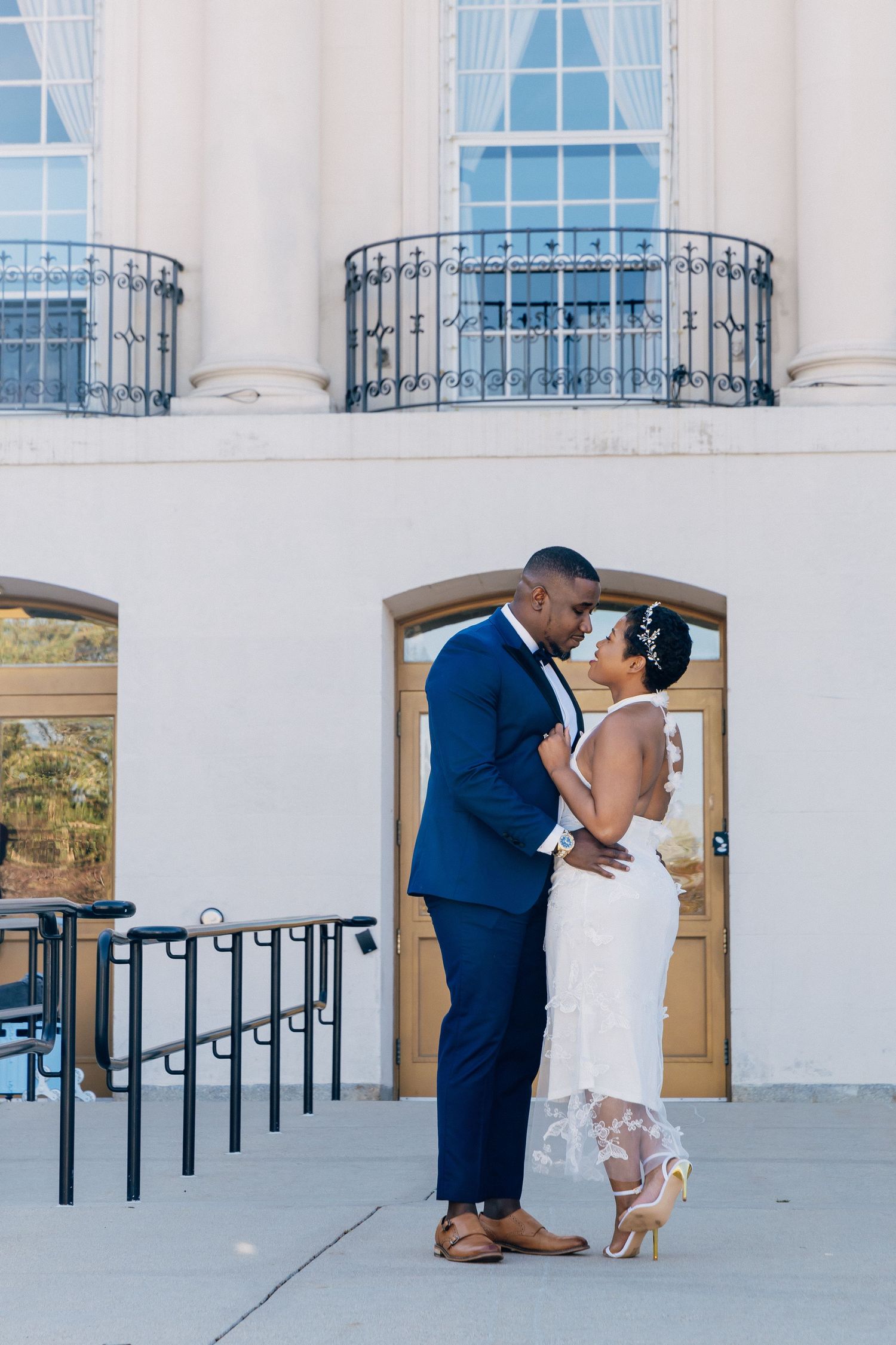 Bride and groom sharing a romantic kiss outside a classic white building with wrought iron balconies.
