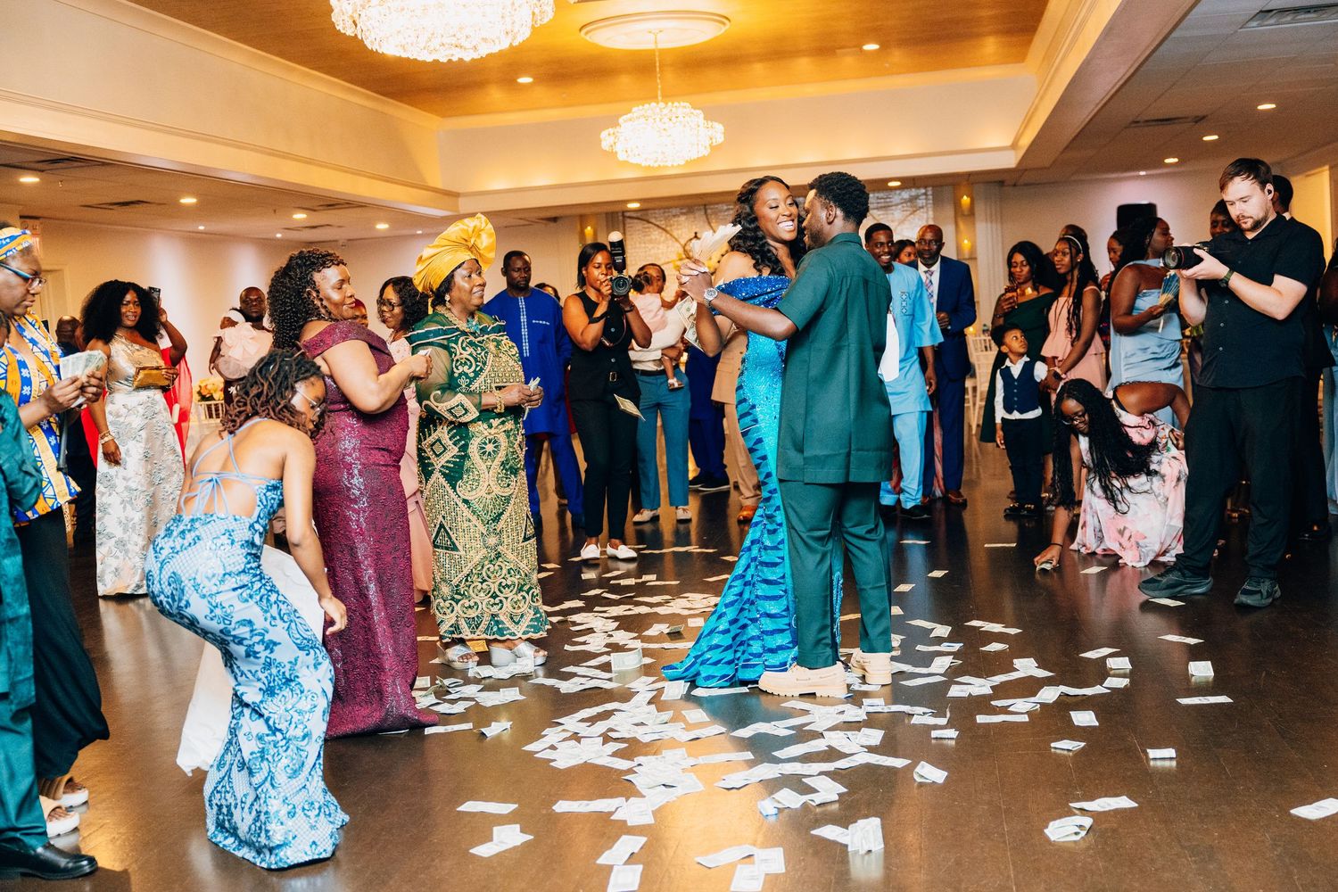 Energetic wedding reception with guests dancing and money scattered across the decorated dance floor.
