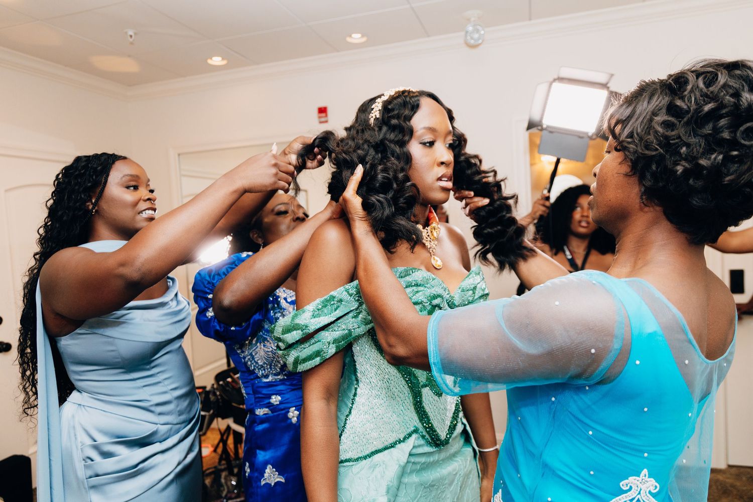 Bridesmaids helping bride get ready, styling her hair in elegant wedding preparation scene.