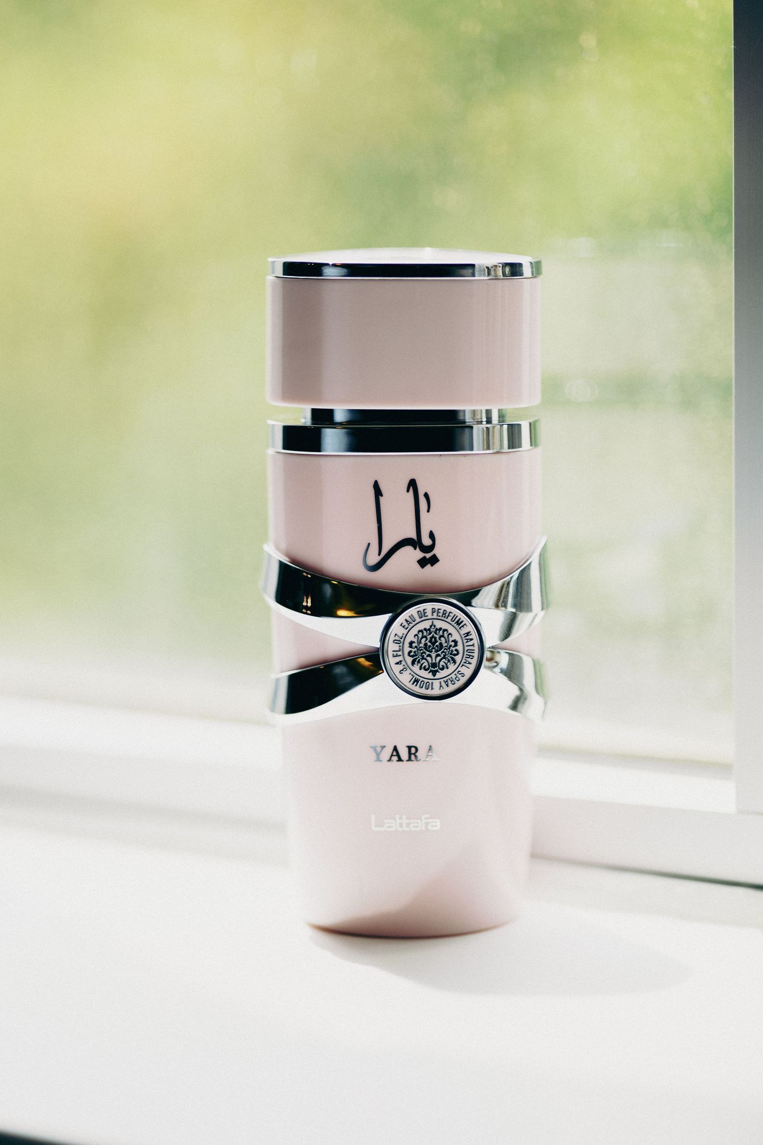 Yara by Lattafa pink perfume bottle with Arabic calligraphy, displayed on a windowsill with natural light.