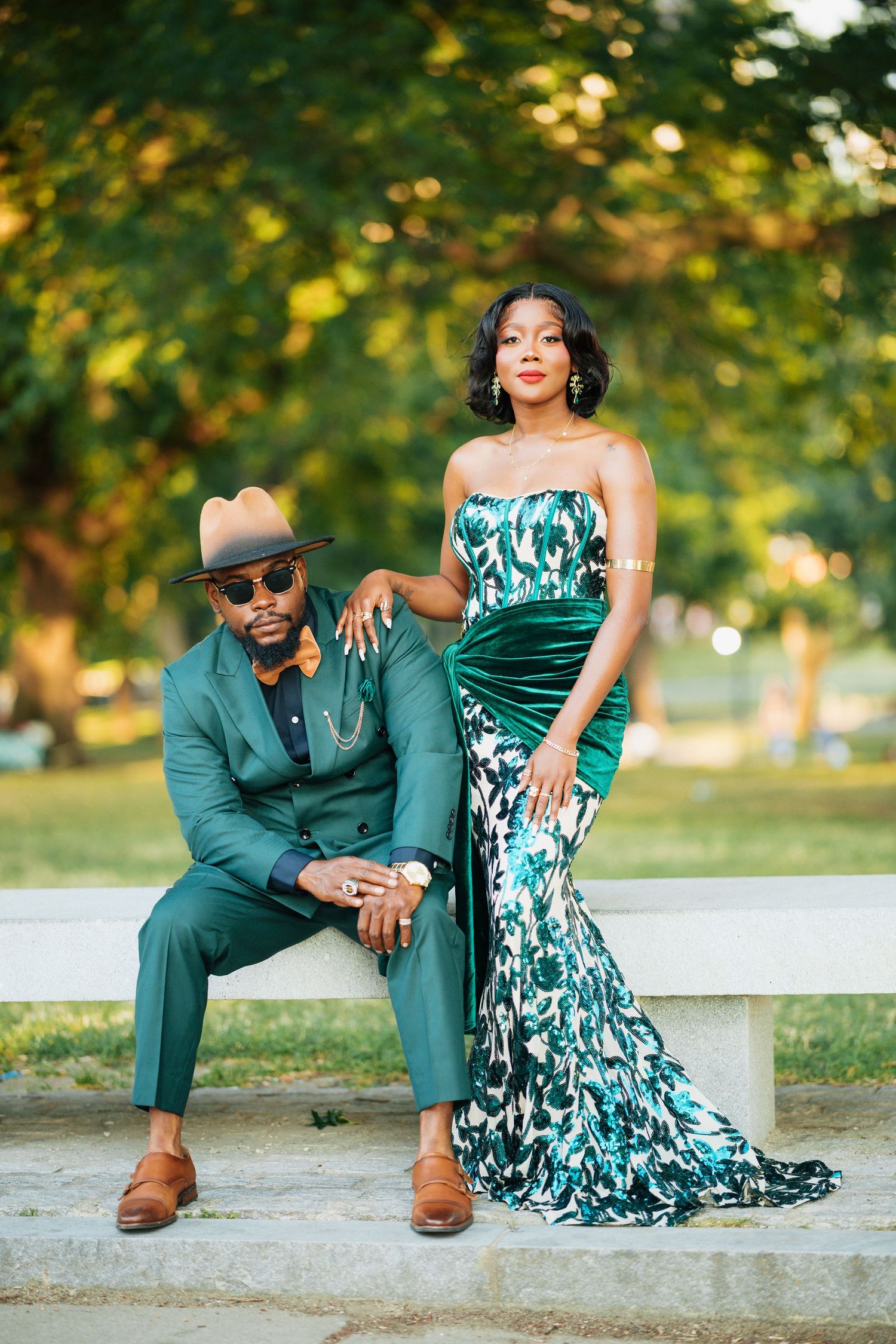 Stylish couple in coordinating emerald green outfits posing on bench in park.