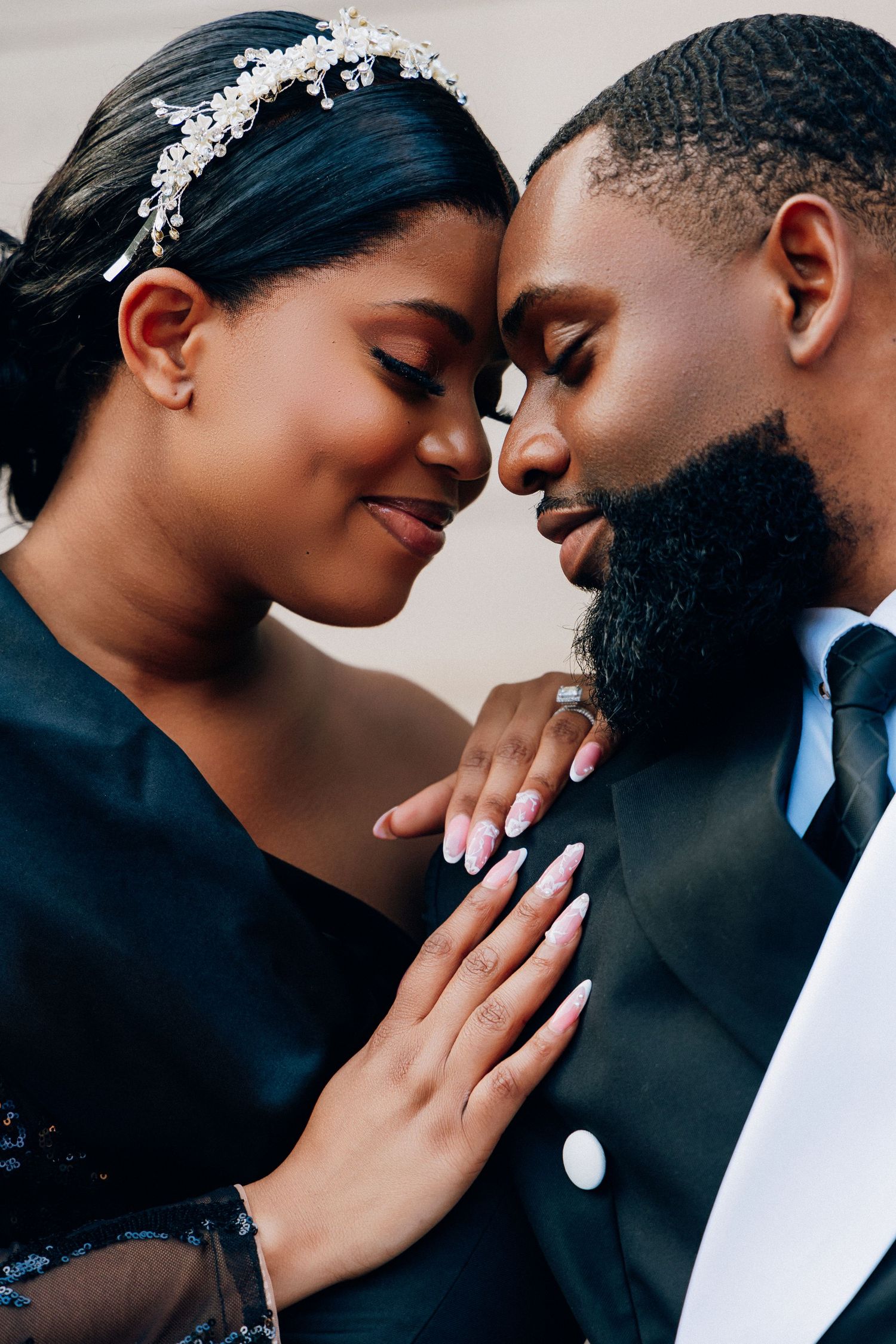 A Black couple in formal wedding attire share a romantic forehead-to-forehead moment, the bride wearing a floral headpiece.