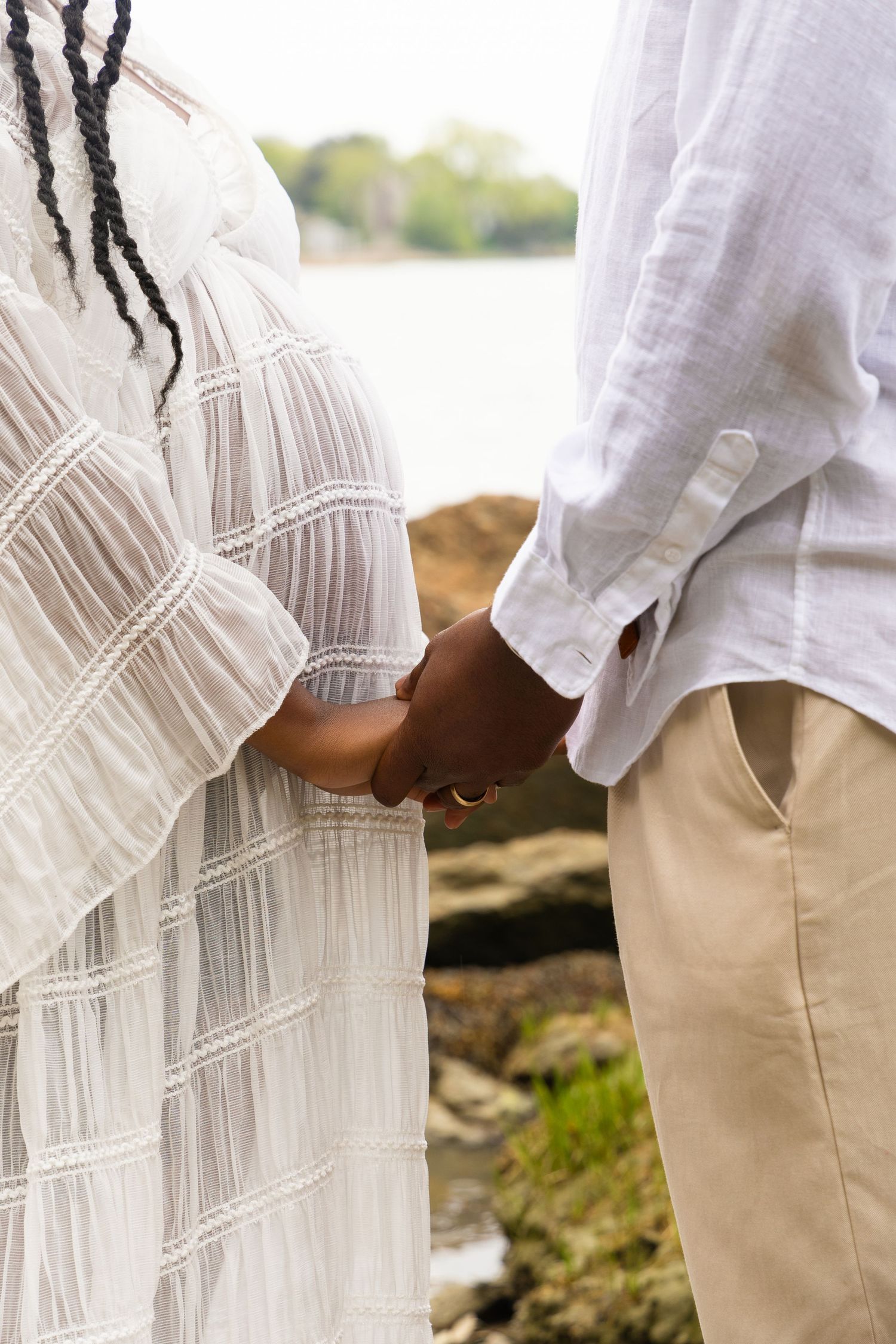 Close-up of a couple holding hands outdoors, woman in white textured dress and man in white linen shirt and khakis.