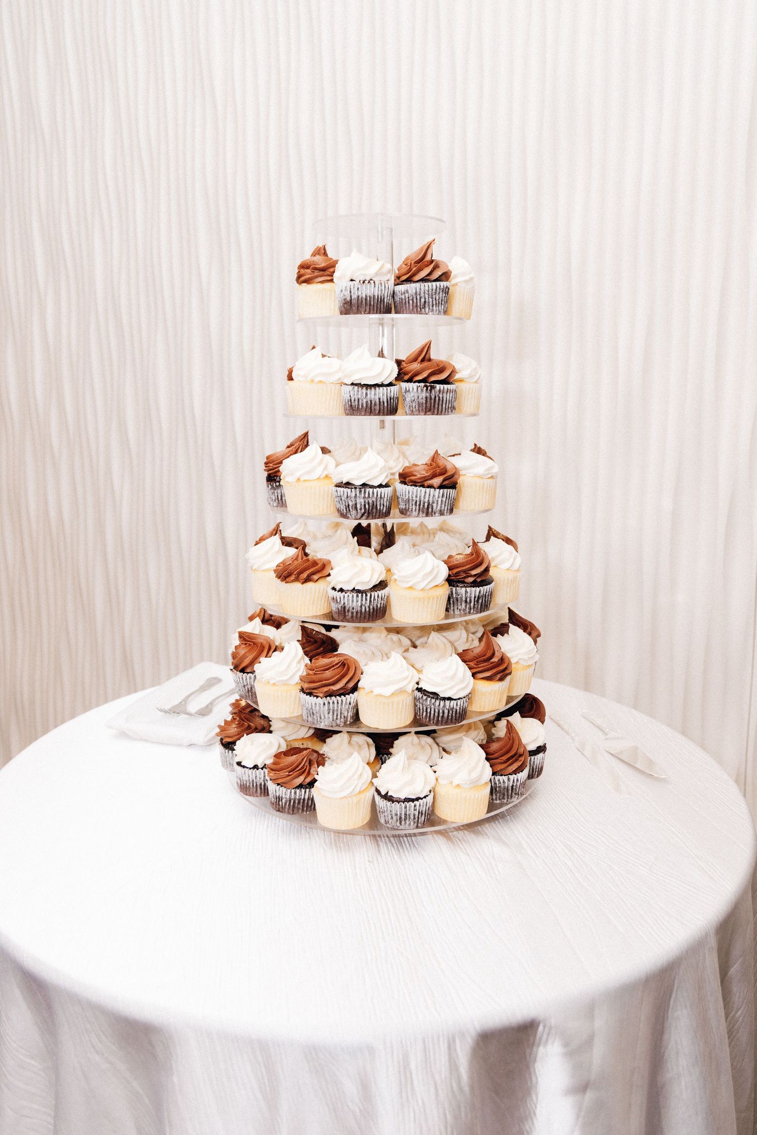 A elegant multi-tiered cupcake tower display featuring chocolate and vanilla frosted cupcakes at a wedding reception.