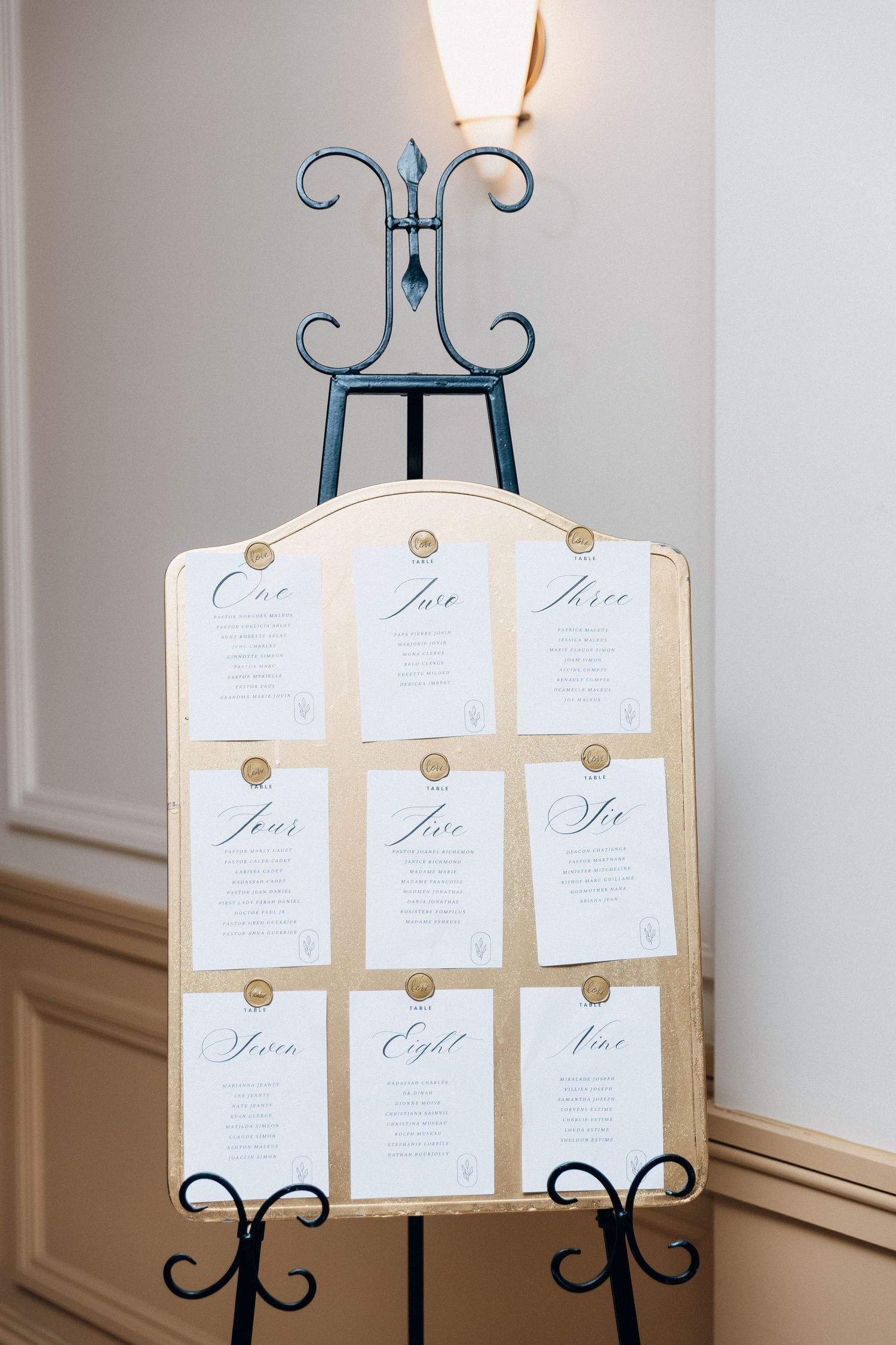 Elegant wedding seating chart displayed on a decorative easel with gold wax seals and calligraphy table numbers.