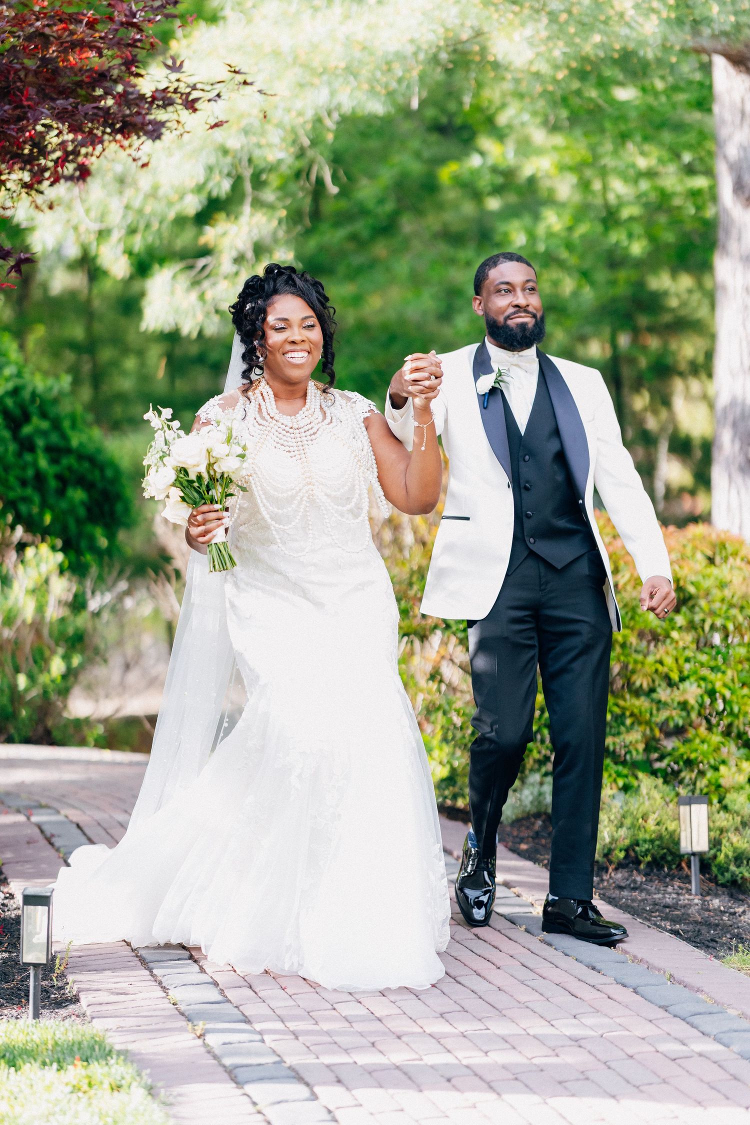 Jubilant newlyweds raise hands in celebration walking down brick path after outdoor wedding ceremony.