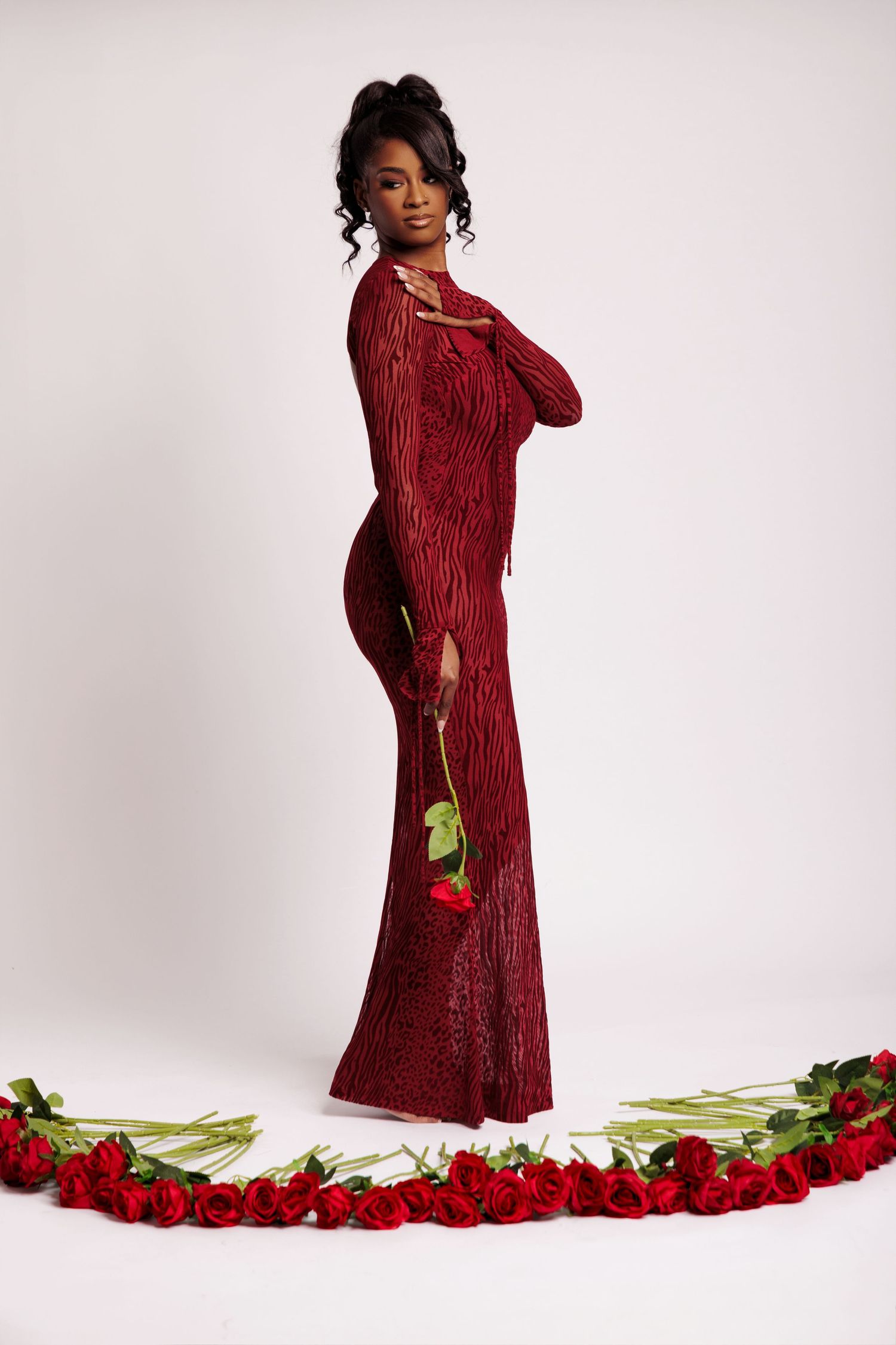Woman in red sequin gown holding a rose, surrounded by red roses arranged in an arc on white background.