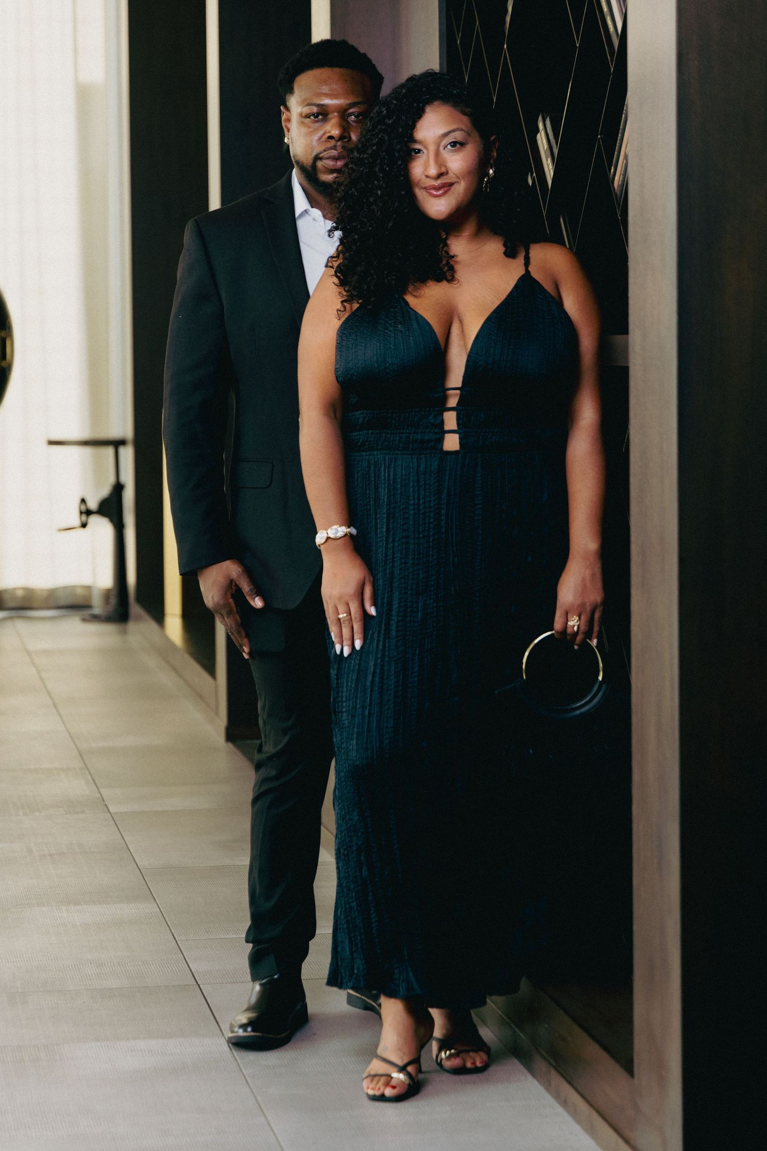 Elegant couple in matching dark green formal attire posing together in a stylish indoor setting.