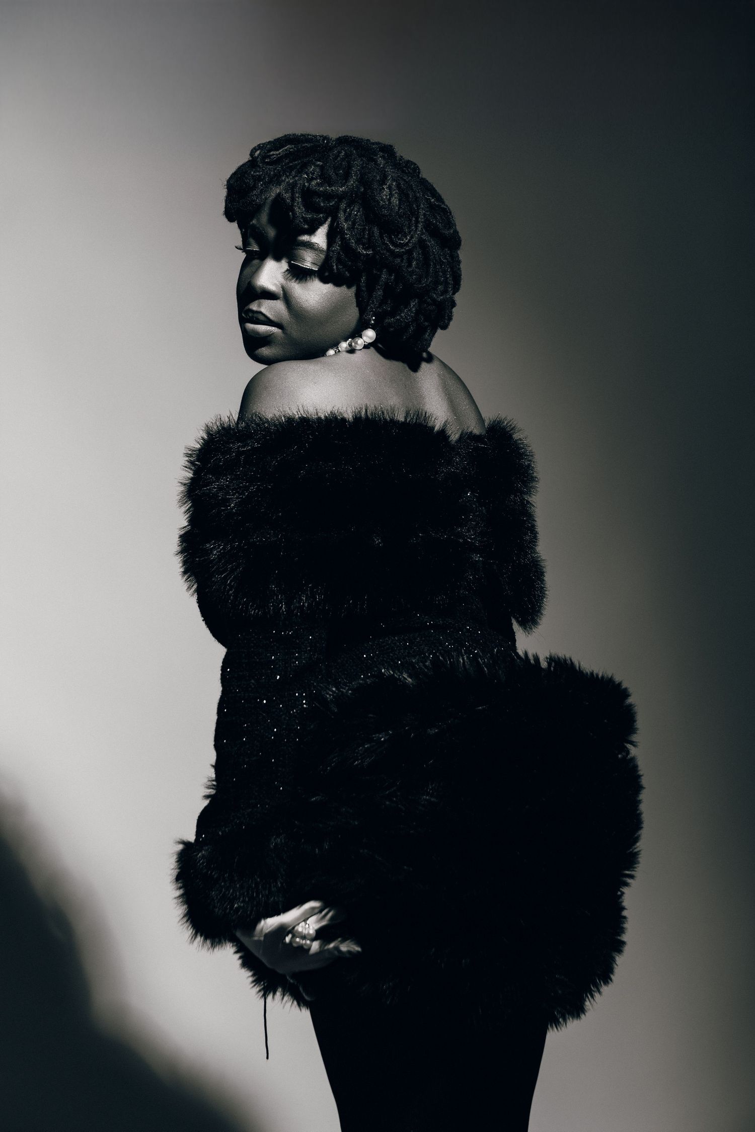 Black and white portrait of a woman in a fur coat posing elegantly against a dramatic studio background.
