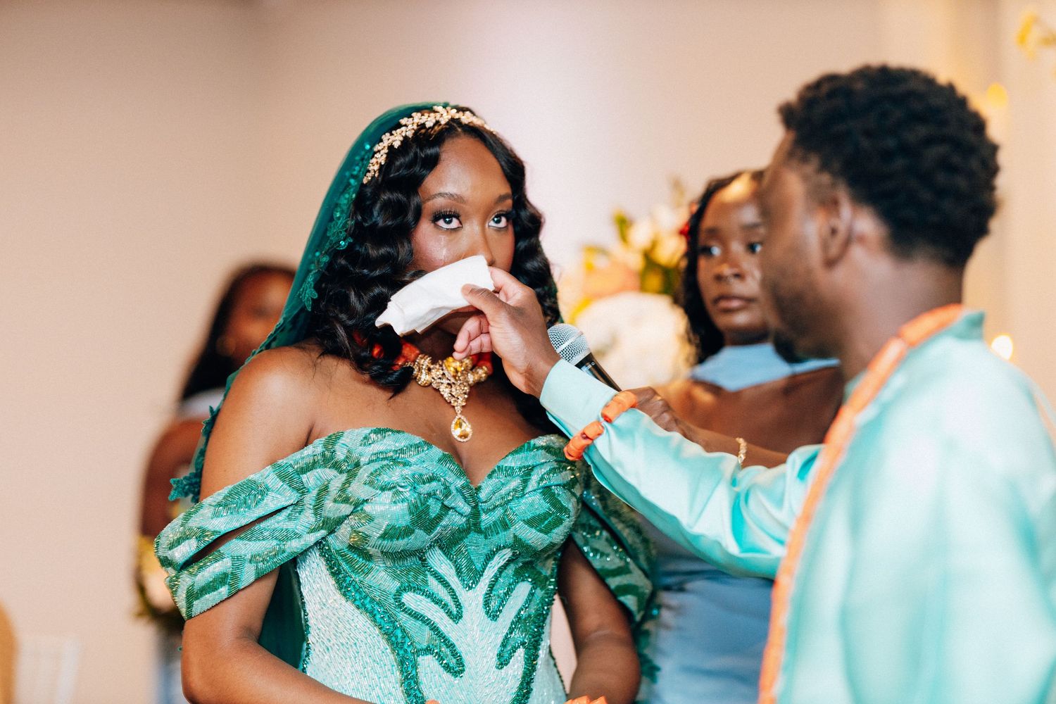 Groom wiping tears from bride's face in green embroidered wedding gown.