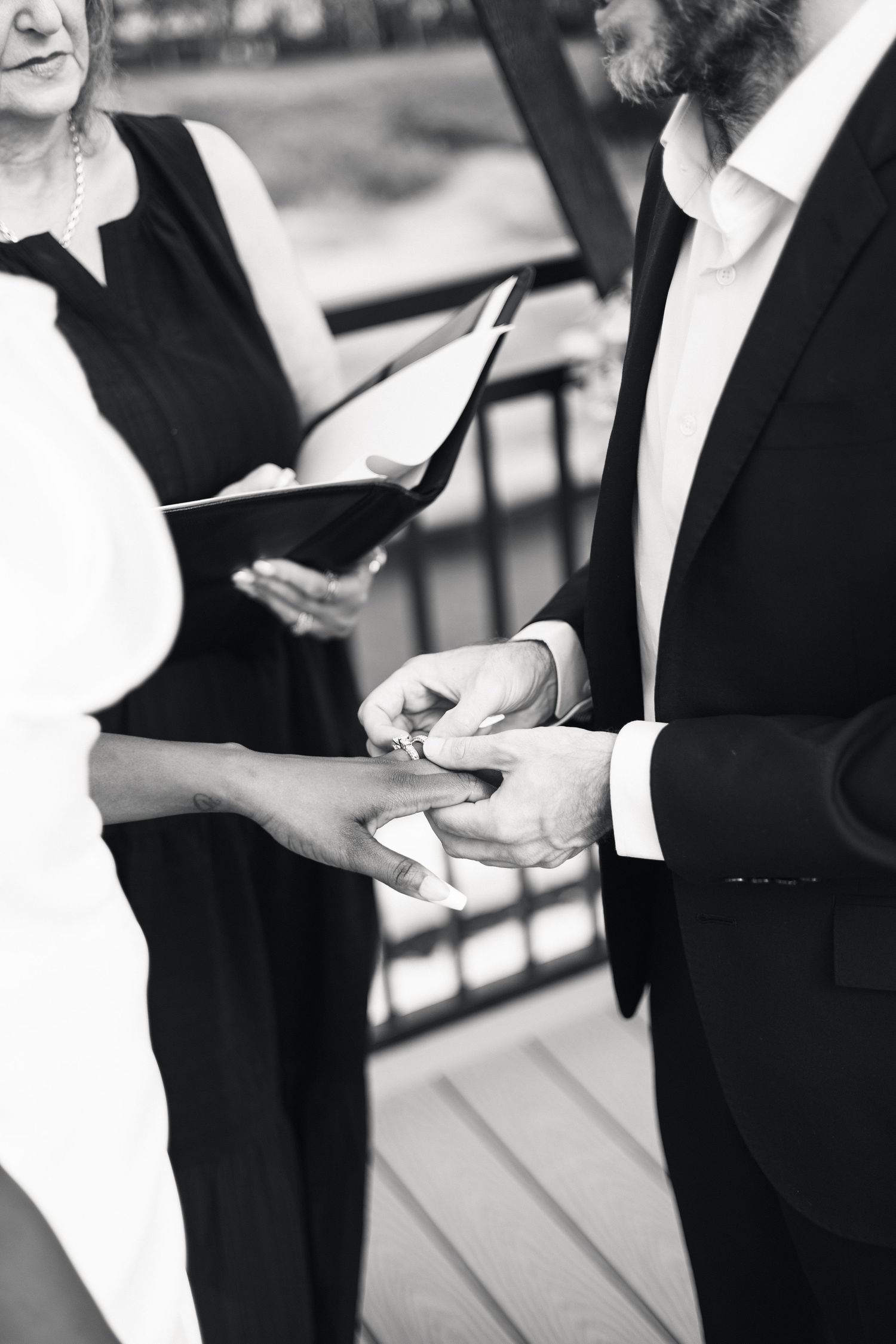 Groom places wedding ring on brides hand during outdoor rooftop ceremony officiated by woman in black.